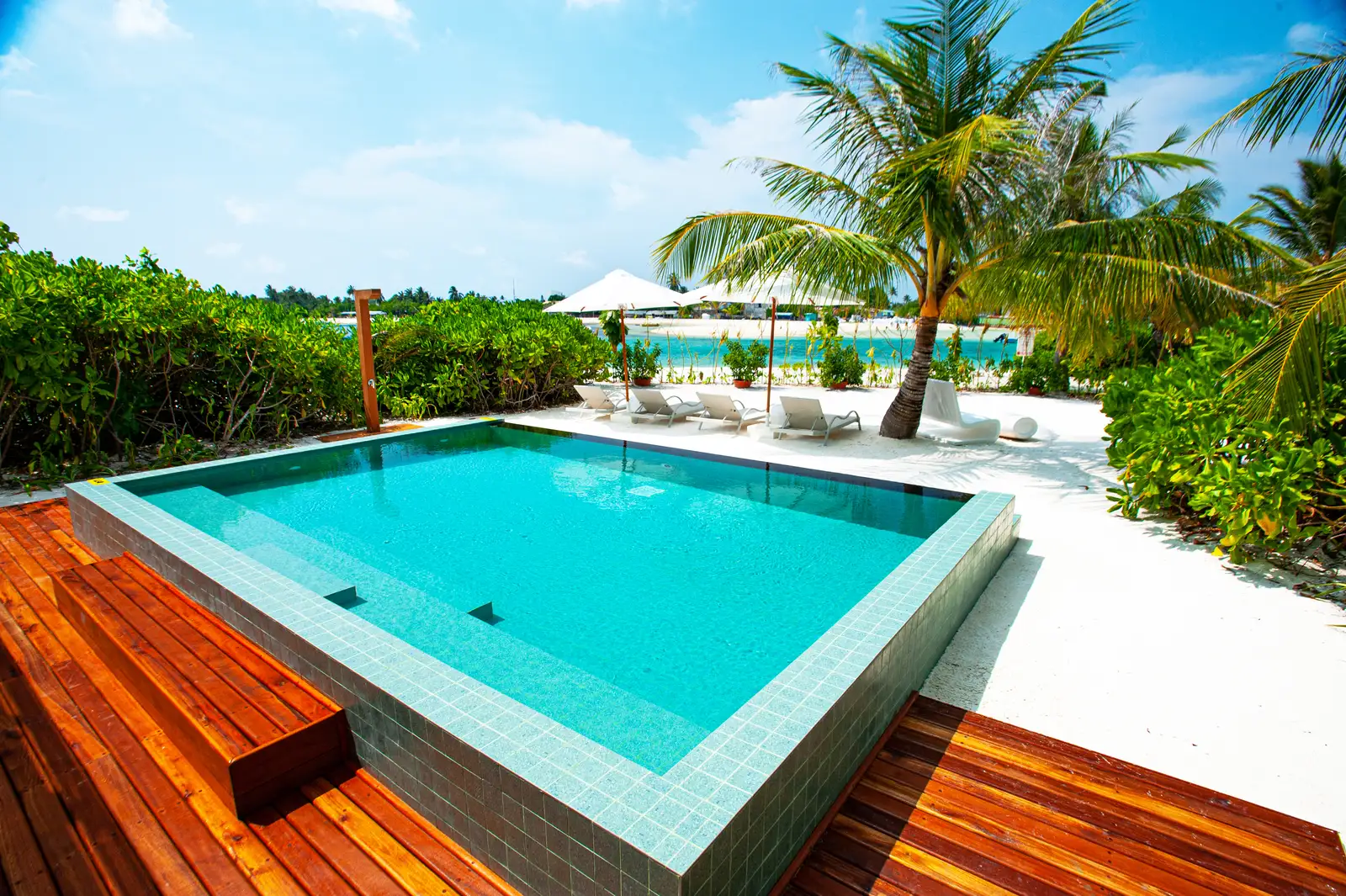 The private pool of a 3-bedroom villa, its timber deck and the palms towards the beach.