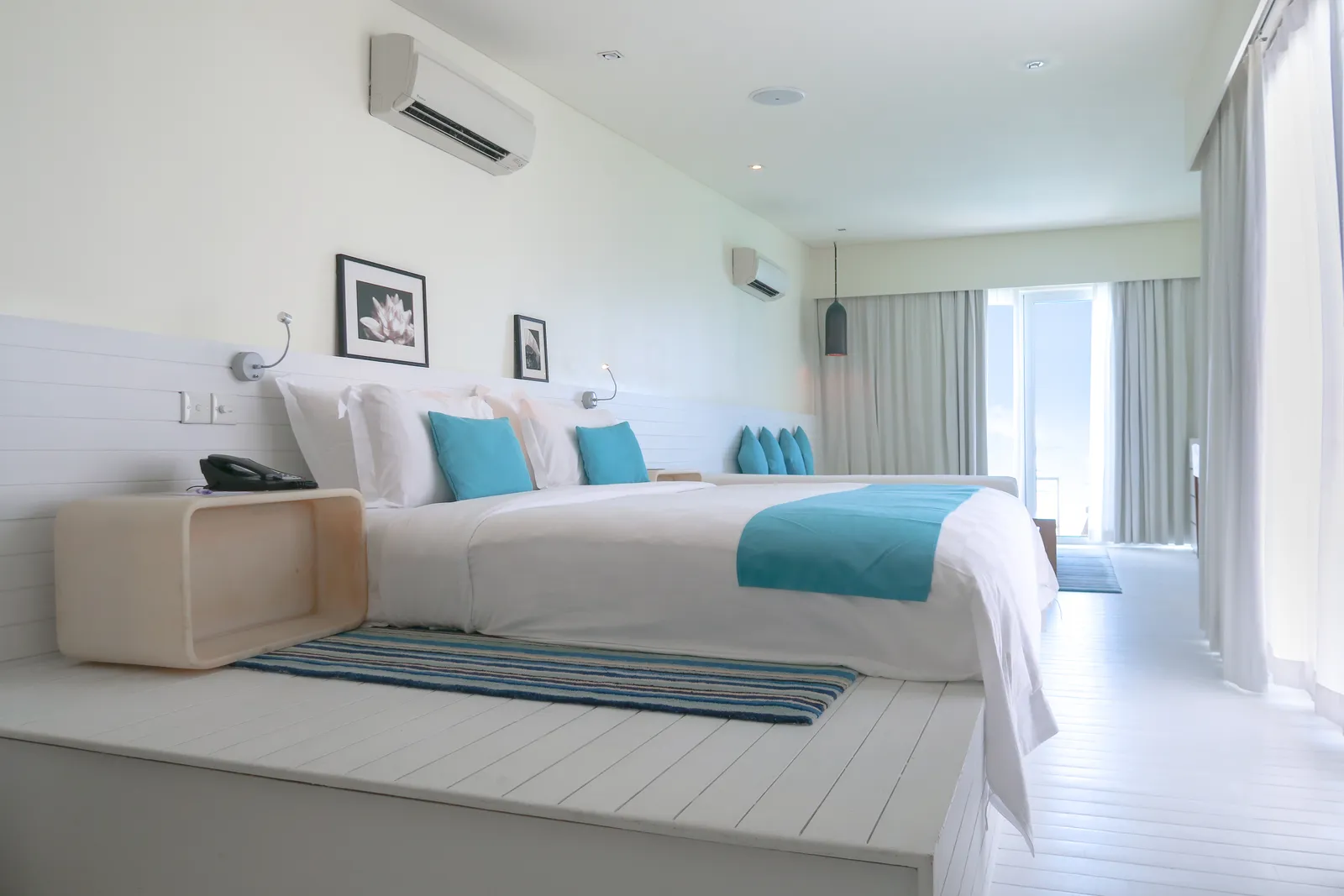 A water villa bedroom, with the king bed, the white bench and the door to the deck.
