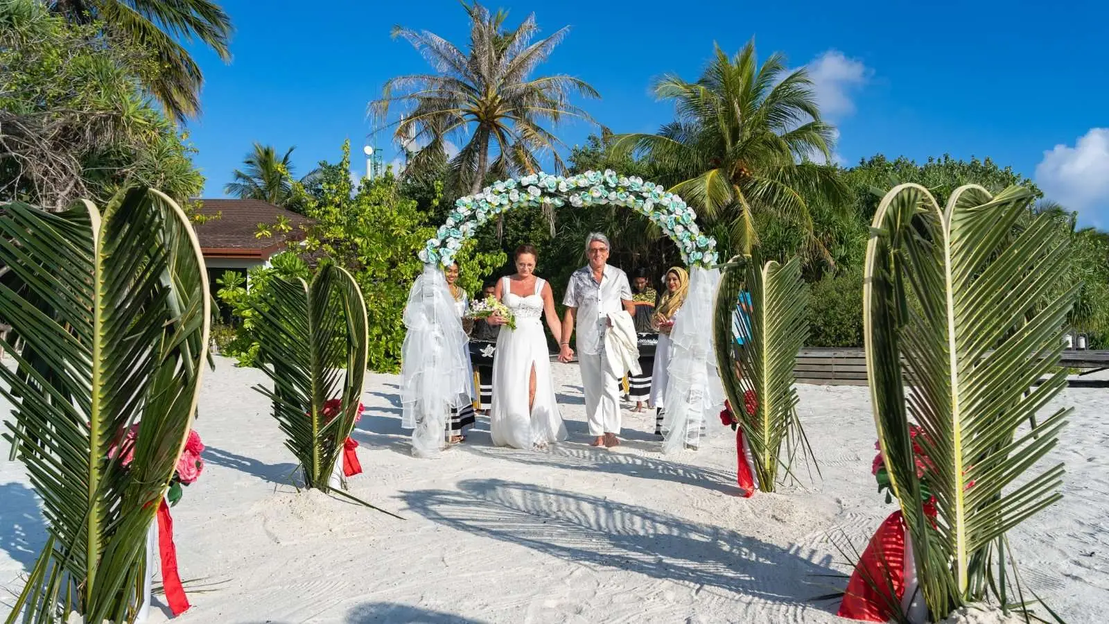 A ceremony on the beach: the couple under the flower arch, between 2 wings of woven palm leaves.