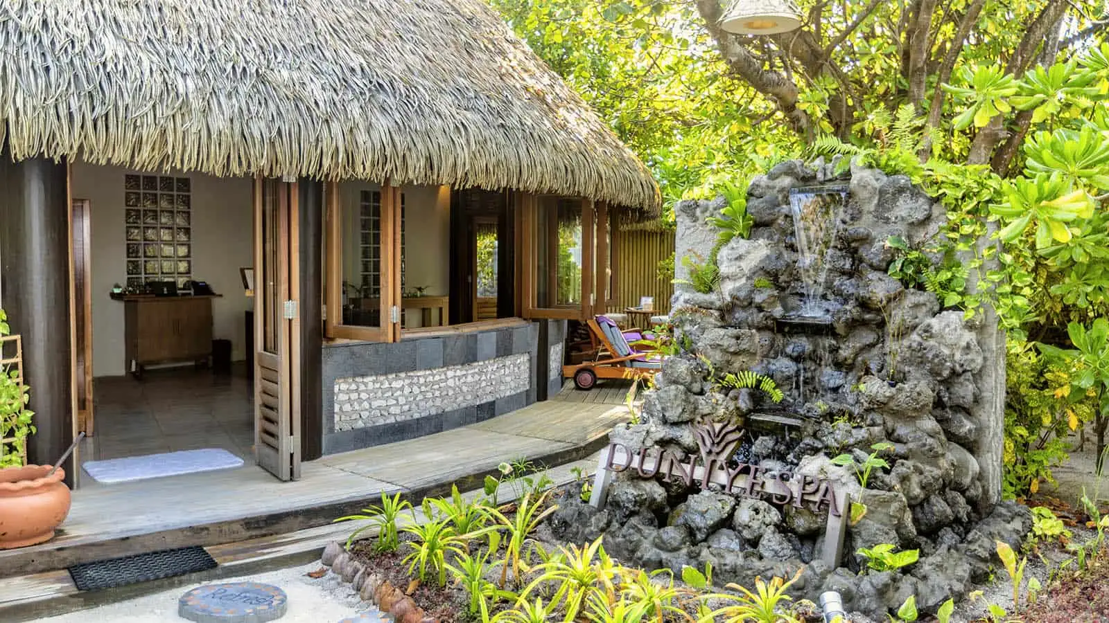 The entrance to Duniye Spa under its thatched roof, with the stone fountain and tropical plants around it.