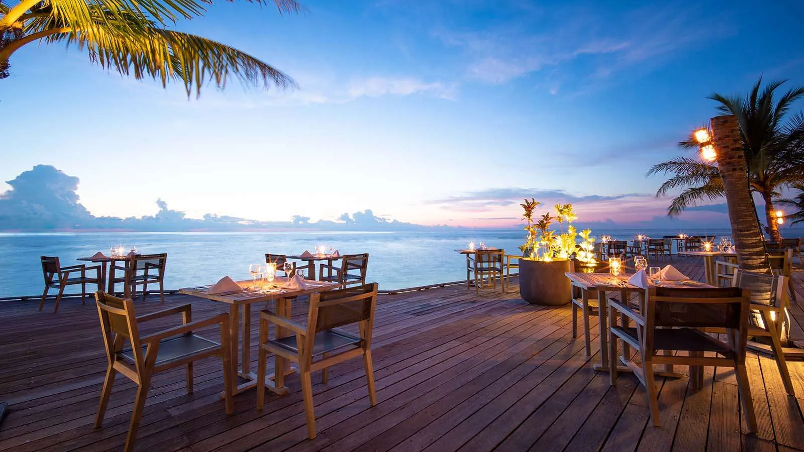 Falhu’s deck over the sea at dusk, with tables laid and candles lit.
