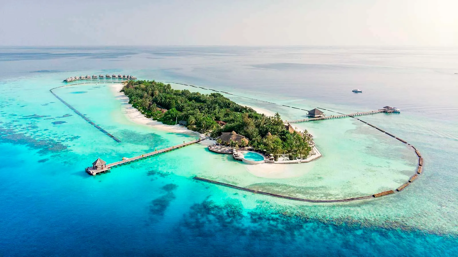 Komandoo from above: the narrow green island, the pale lagoon around it and the jetties of the water villas.