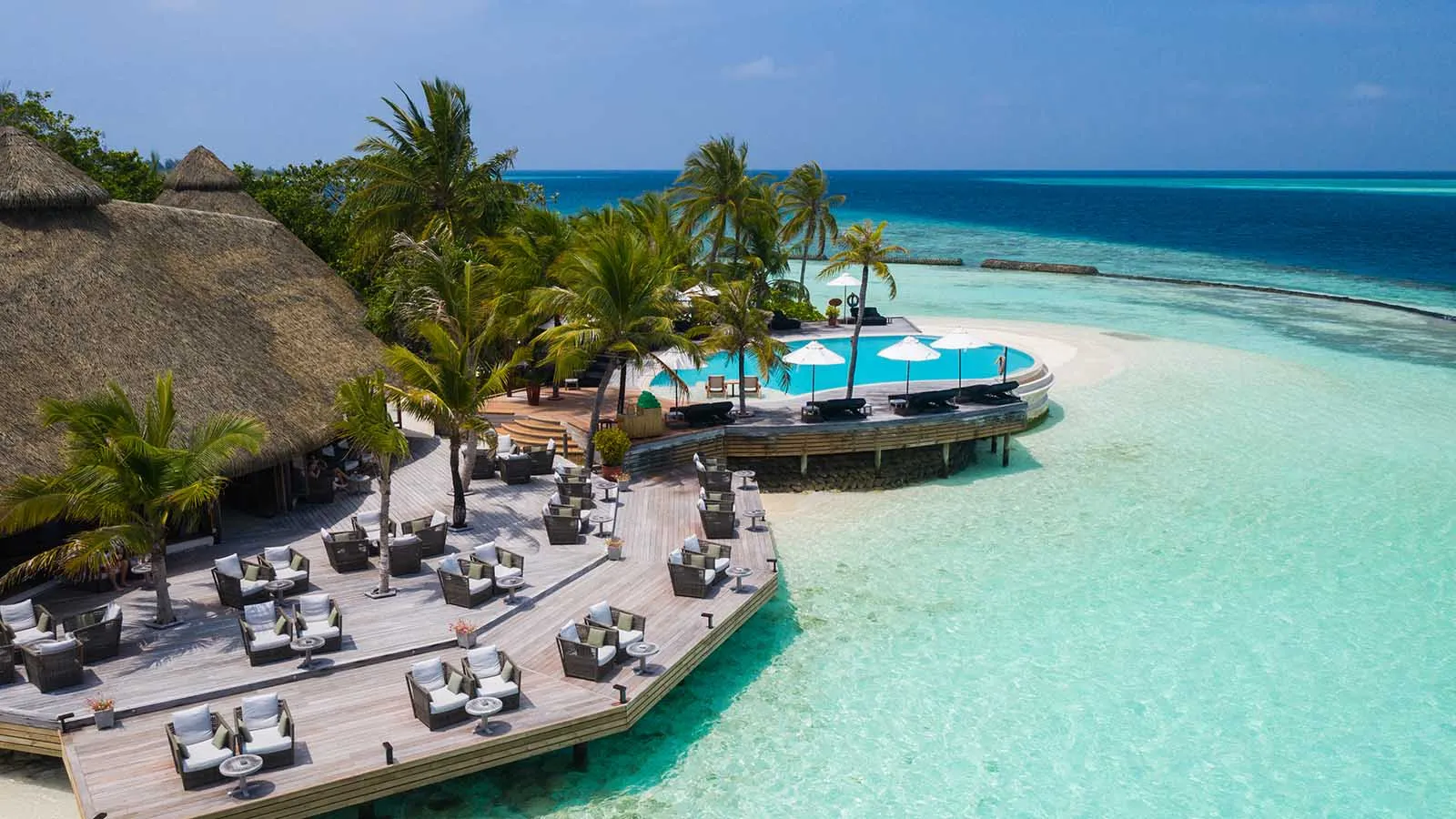 The Kandu Bar deck from above, with its sofas, the infinity pool beside it and the turquoise lagoon.