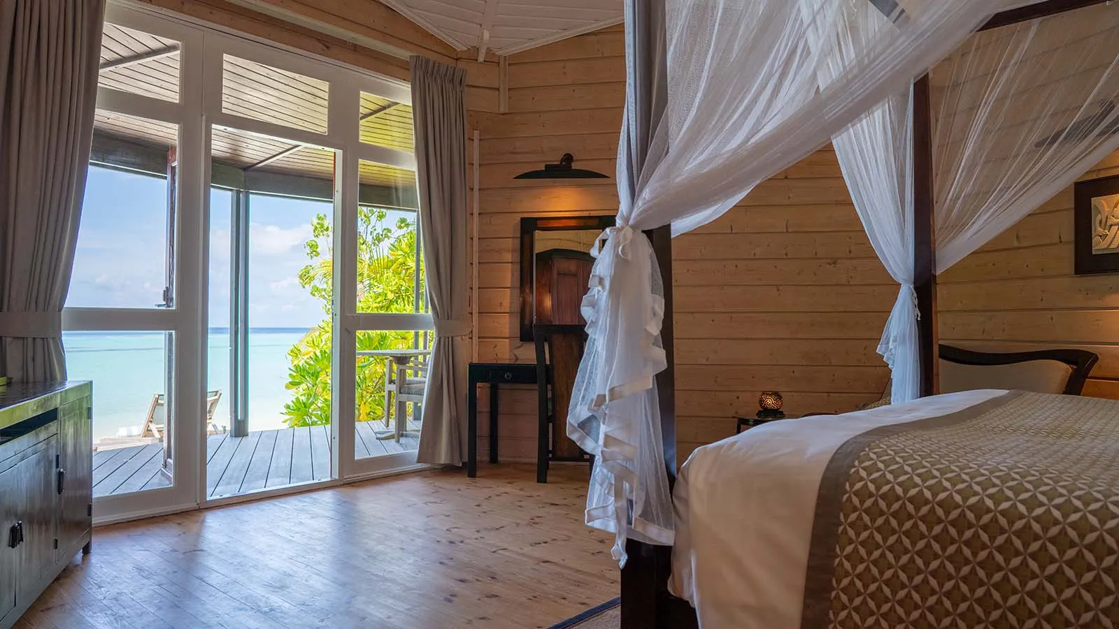 Inside a Beach Villa: the bed under its mosquito net, the timber walls and the glass door open onto the veranda.