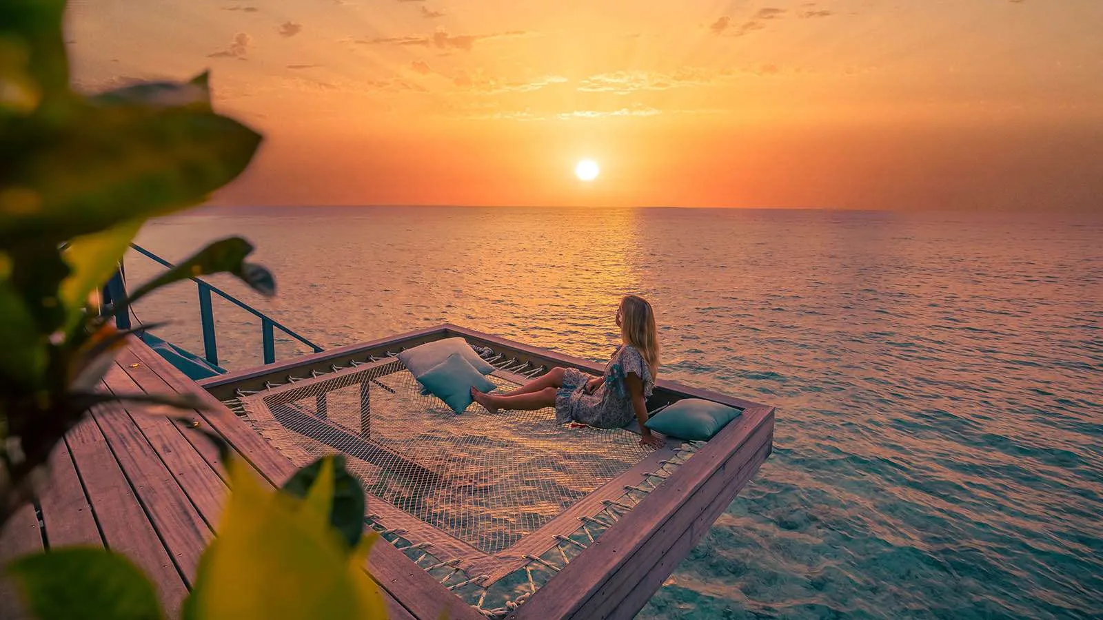 The catamaran net on an Ocean Jacuzzi Water Villa’s deck, a guest stretched out facing the low sun over the sea.