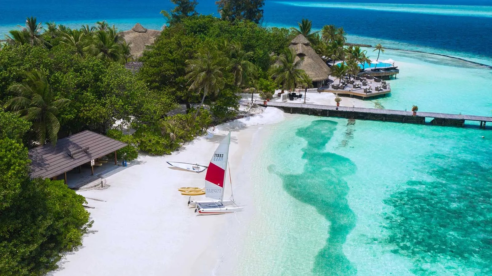 The water sports beach from above, with a catamaran drawn up on the sand and the jetty over the lagoon.
