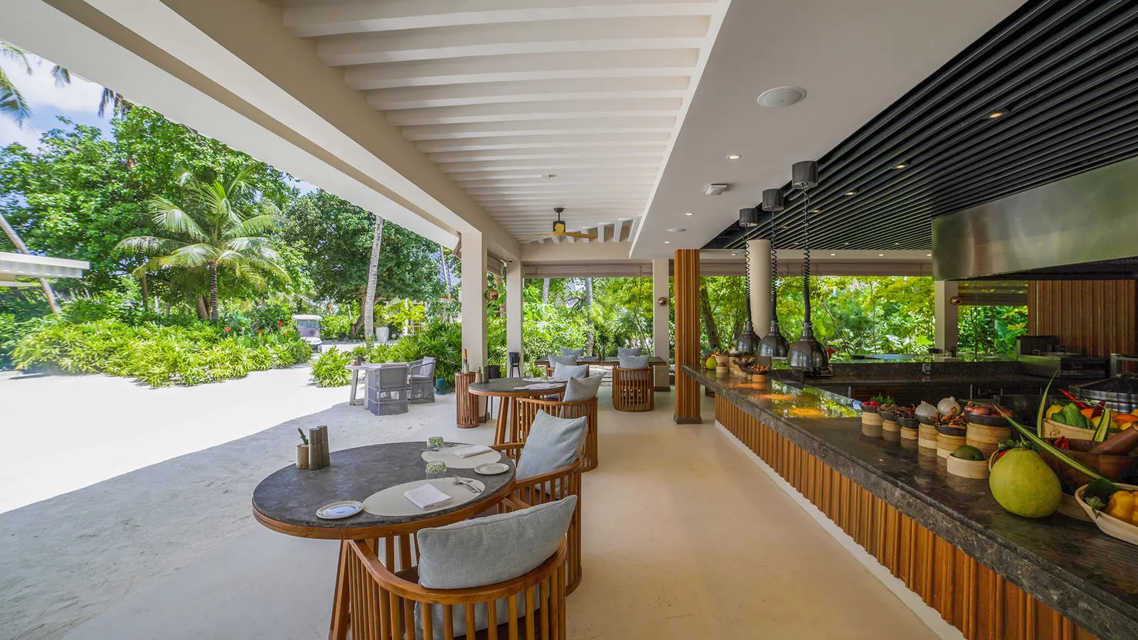 East's covered terrace, with its round tables, the open kitchen and the sand beyond the columns.