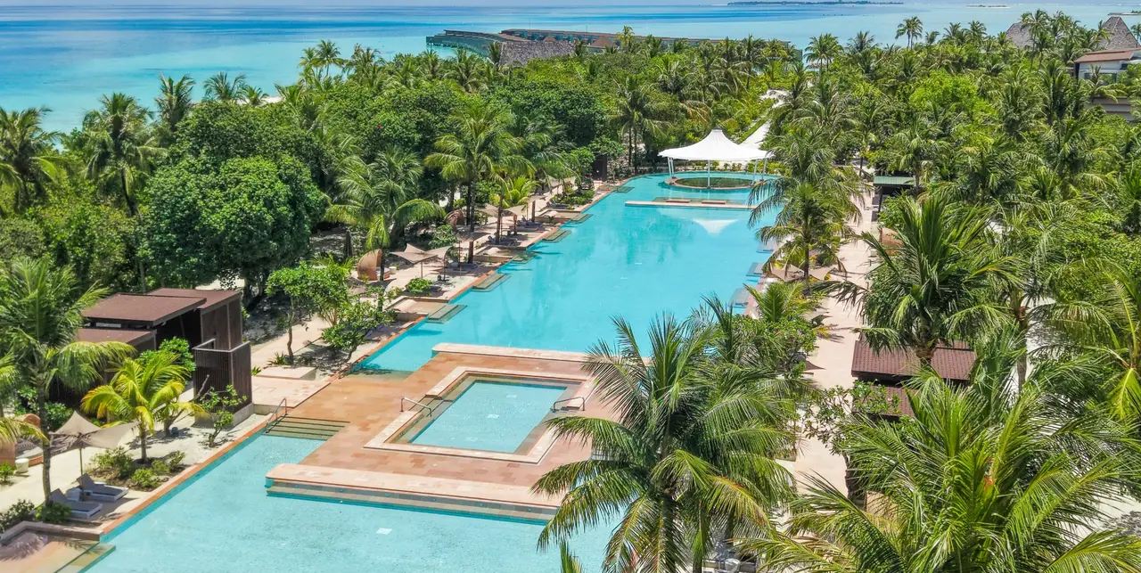 The 150-metre central pool from above, running between the palms, with its shallow basin and the white canopy in the middle.