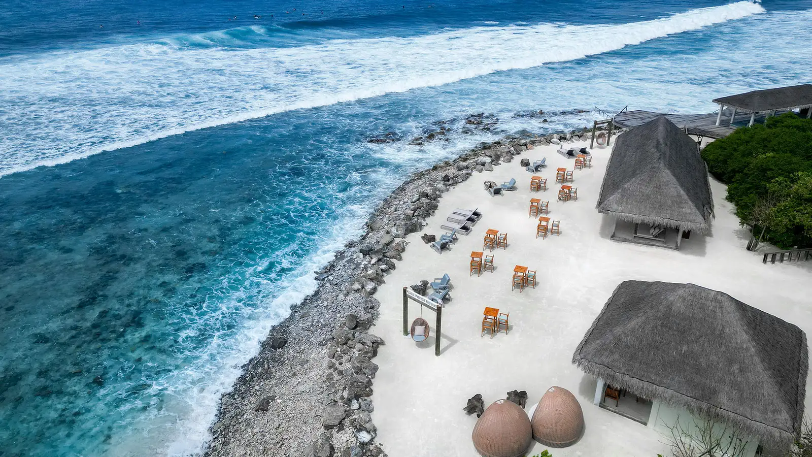 Raalhu Bar from above: tables on the sand, the thatched huts and the waves breaking on the reef.