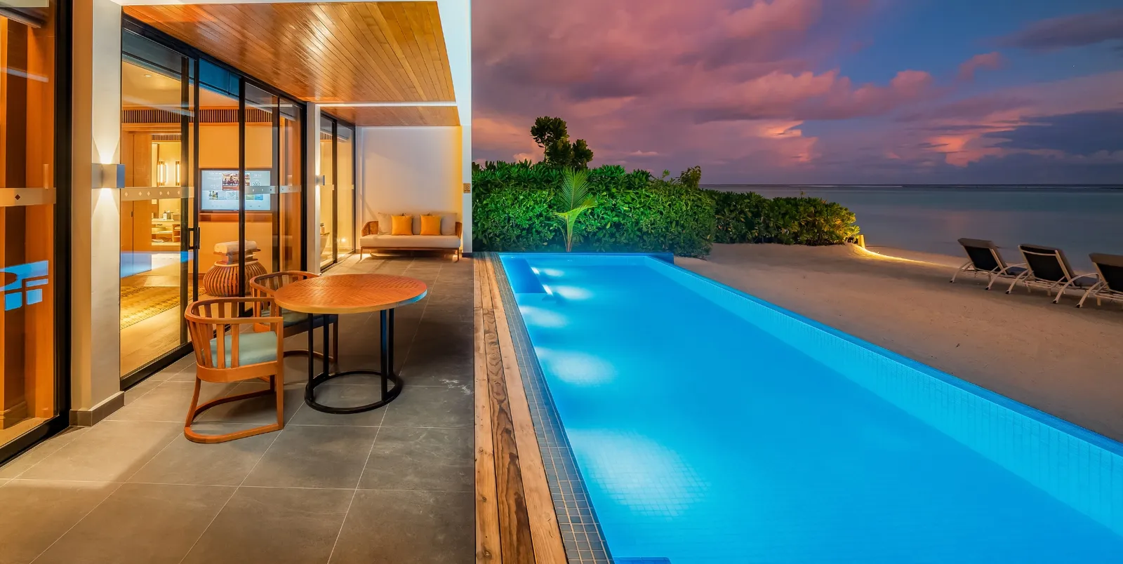 The open-air living room of the Four Bedroom Beach Residence and its long pool, lit at sunset.