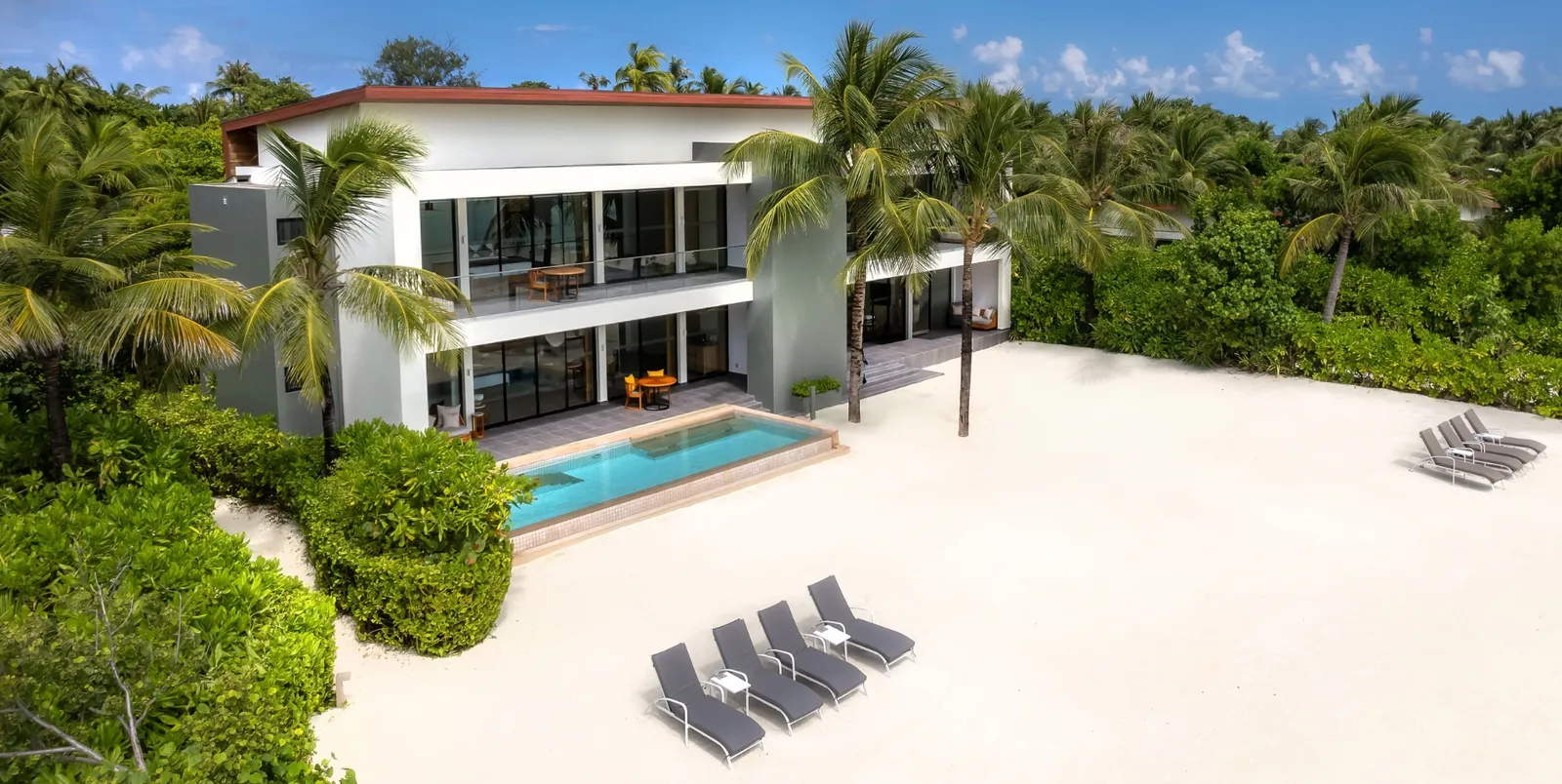 The Four Bedroom Beach Villa from above: the 2-storey white house, the pool and the loungers on the sand.