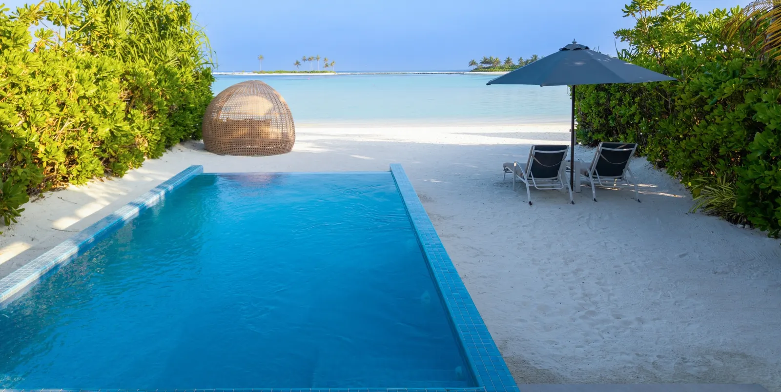 A Sunrise Beach Villa's pool running out to the sand, with the domed daybed and the parasol.
