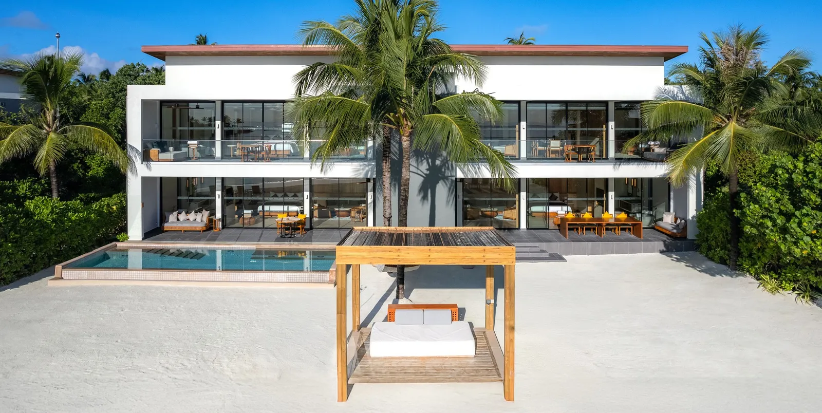 The Three Bedroom Beach Residence seen from the beach: 2 white storeys, the pool and the canopy daybed.