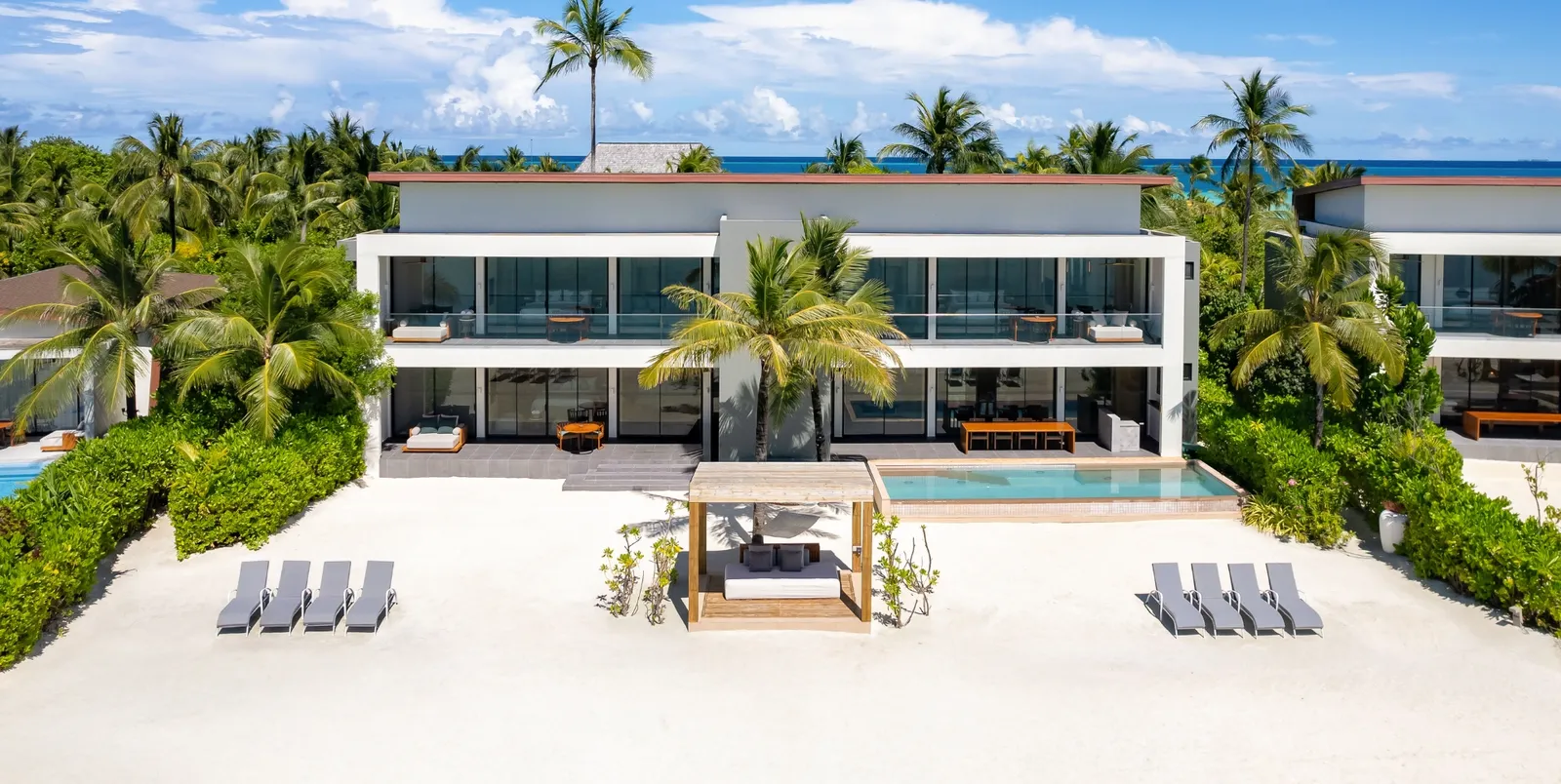 The Three Bedroom Beach Retreat from above, with the long pool, the loungers on the sand and the greenery around it.