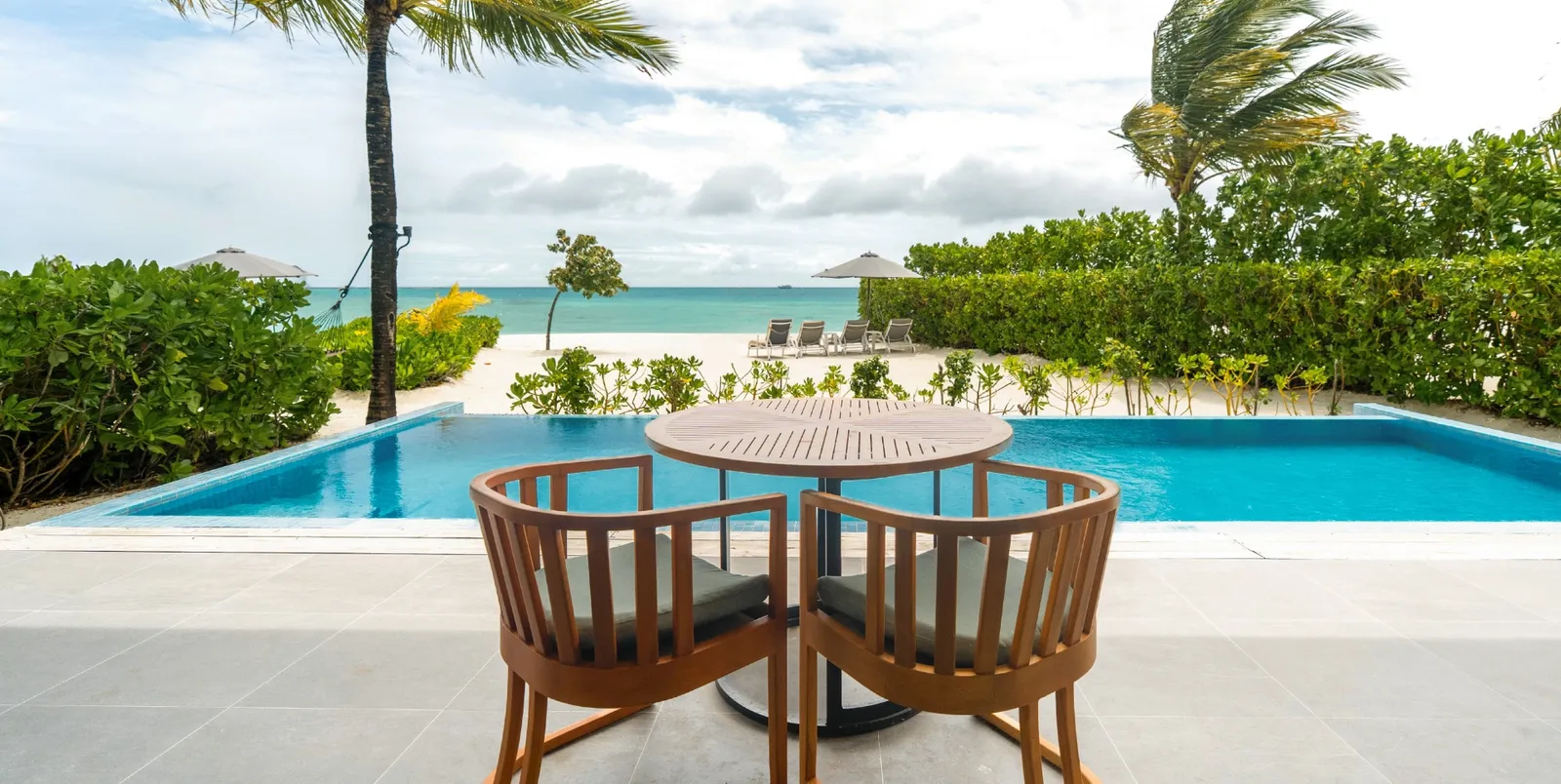 The outdoor table by the pool of the Two Bedroom Beach Residence, with the beach beyond the hedge.