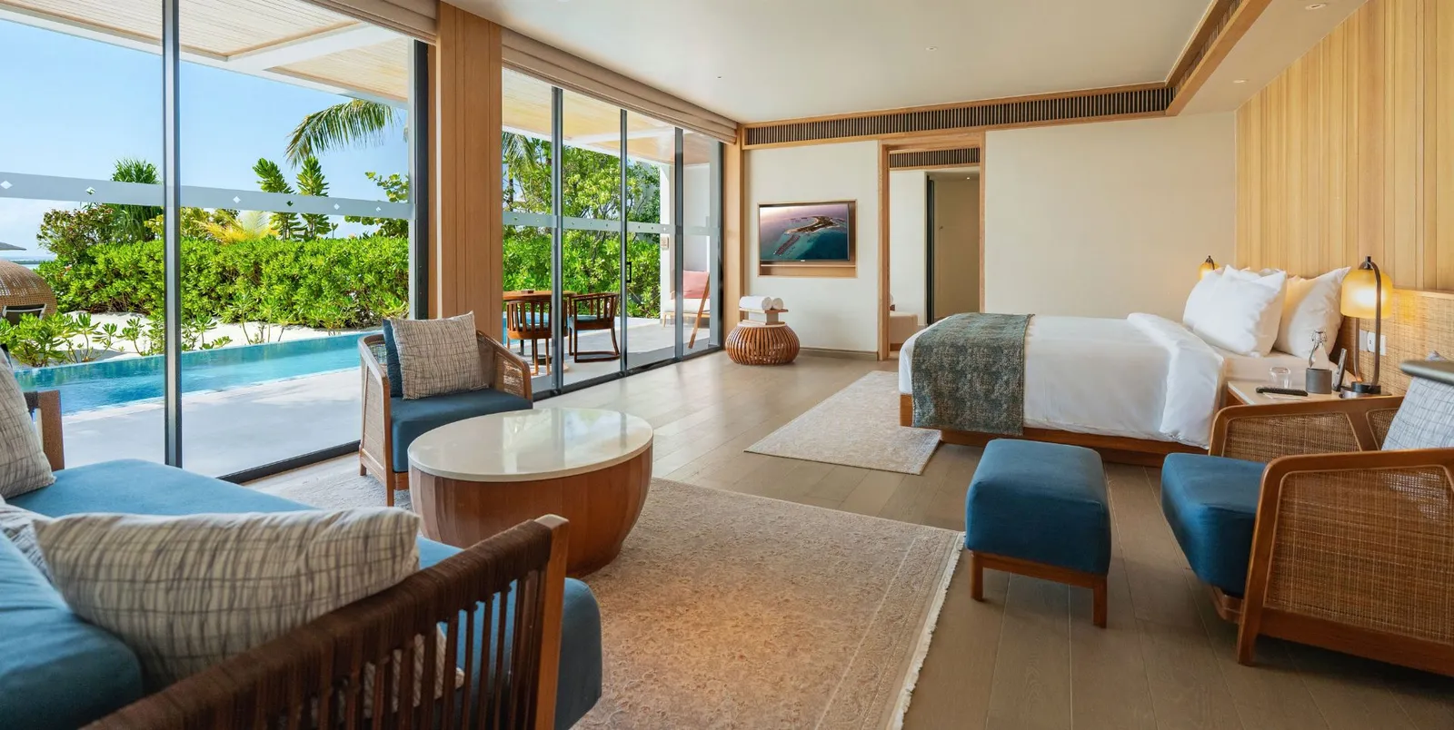 A bedroom of the Two Bedroom Beach Villa, with the bed, the sofa and glass doors onto the pool.