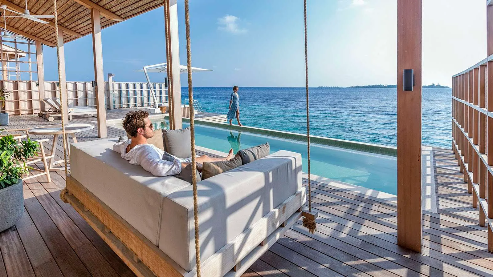 A guest on the hanging daybed of a residence deck, the pool and the open sea ahead