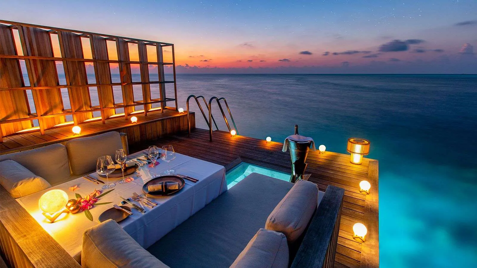 A residence deck at dusk, the pool lit and a table laid