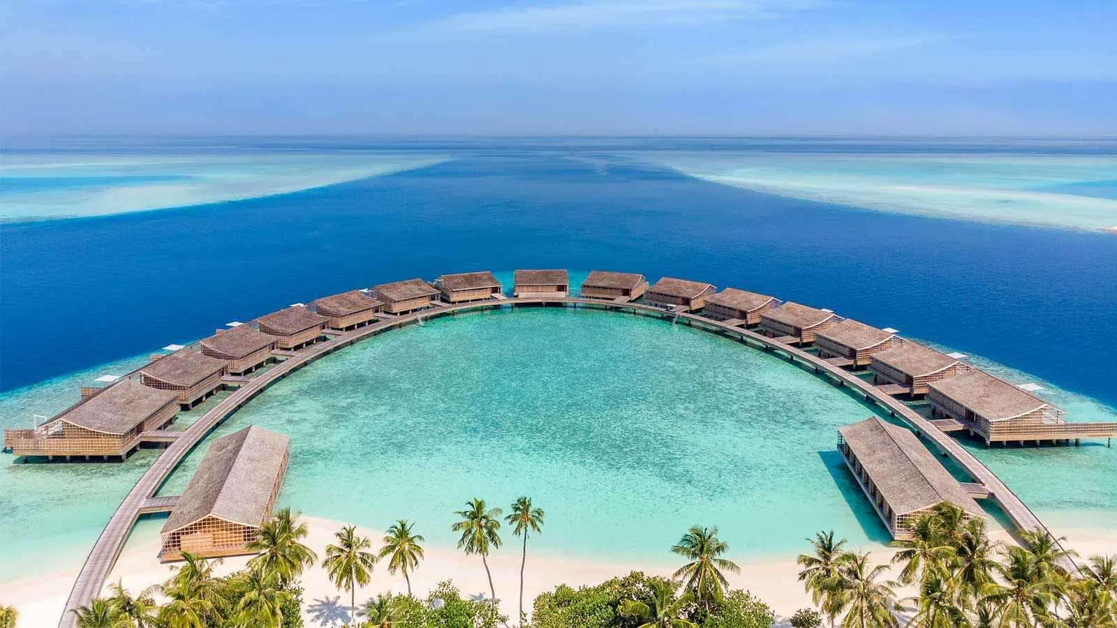 The arc of overwater residences seen from the island, the turquoise lagoon inside it