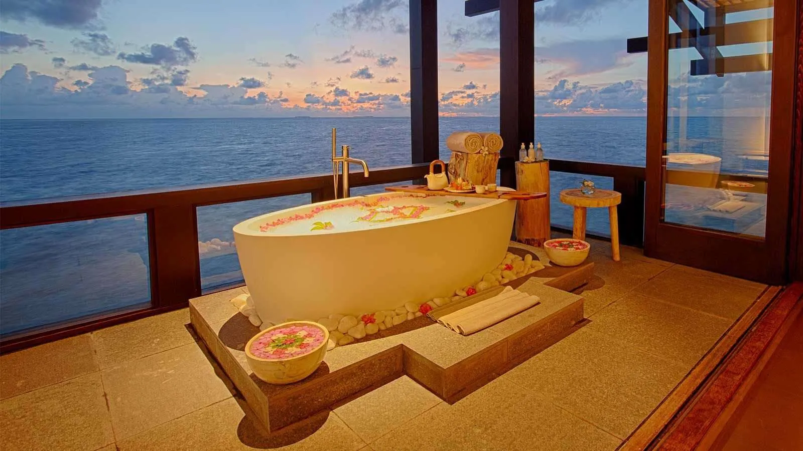 A bath strewn with petals in a spa room, the sea beyond the glass