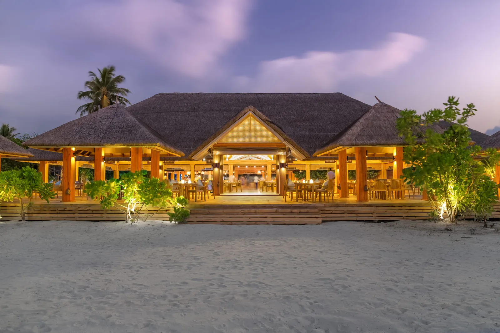 De’ North at dusk: the thatched pavilion lit up, with the sand in front.
