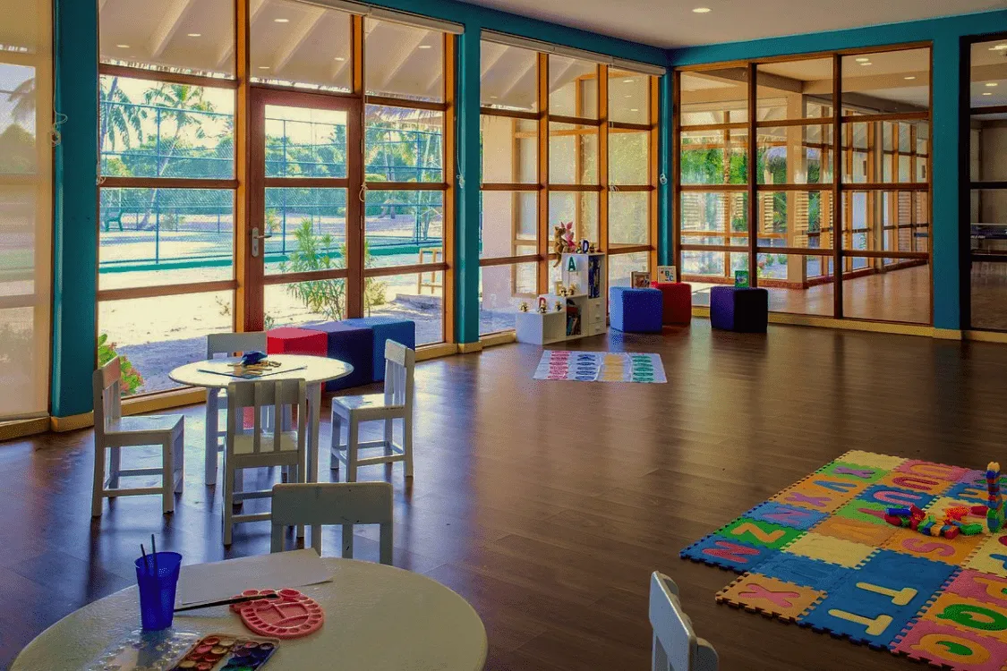 The Little Bubbles Club room, with small tables, white chairs, bright play mats and windows on the garden.