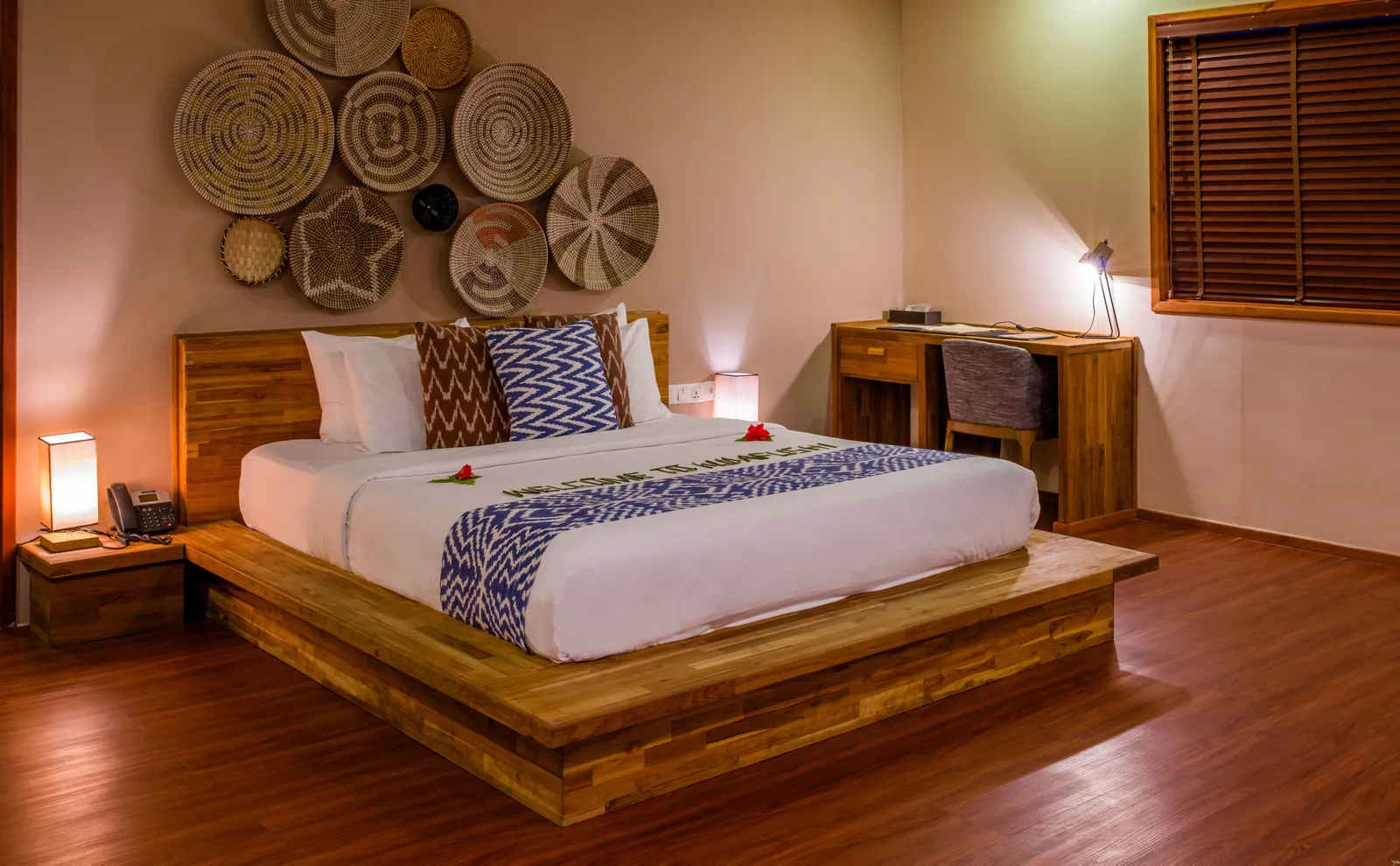 A Presidential Suite bedroom: the bed on a timber platform, woven baskets hung on the wall and the desk.