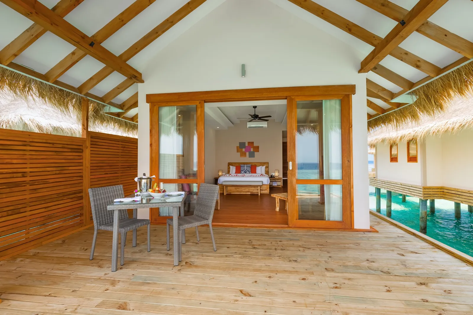A Water Villa’s terrace with a laid table and, through the door, the bedroom with its bed and ceiling fan.