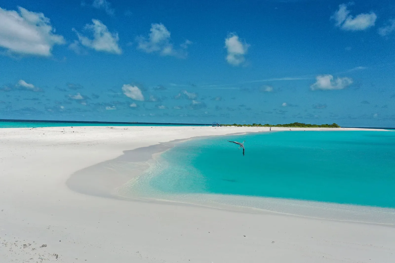 A white sandbank stretching into the turquoise lagoon, under a sky with a few clouds.