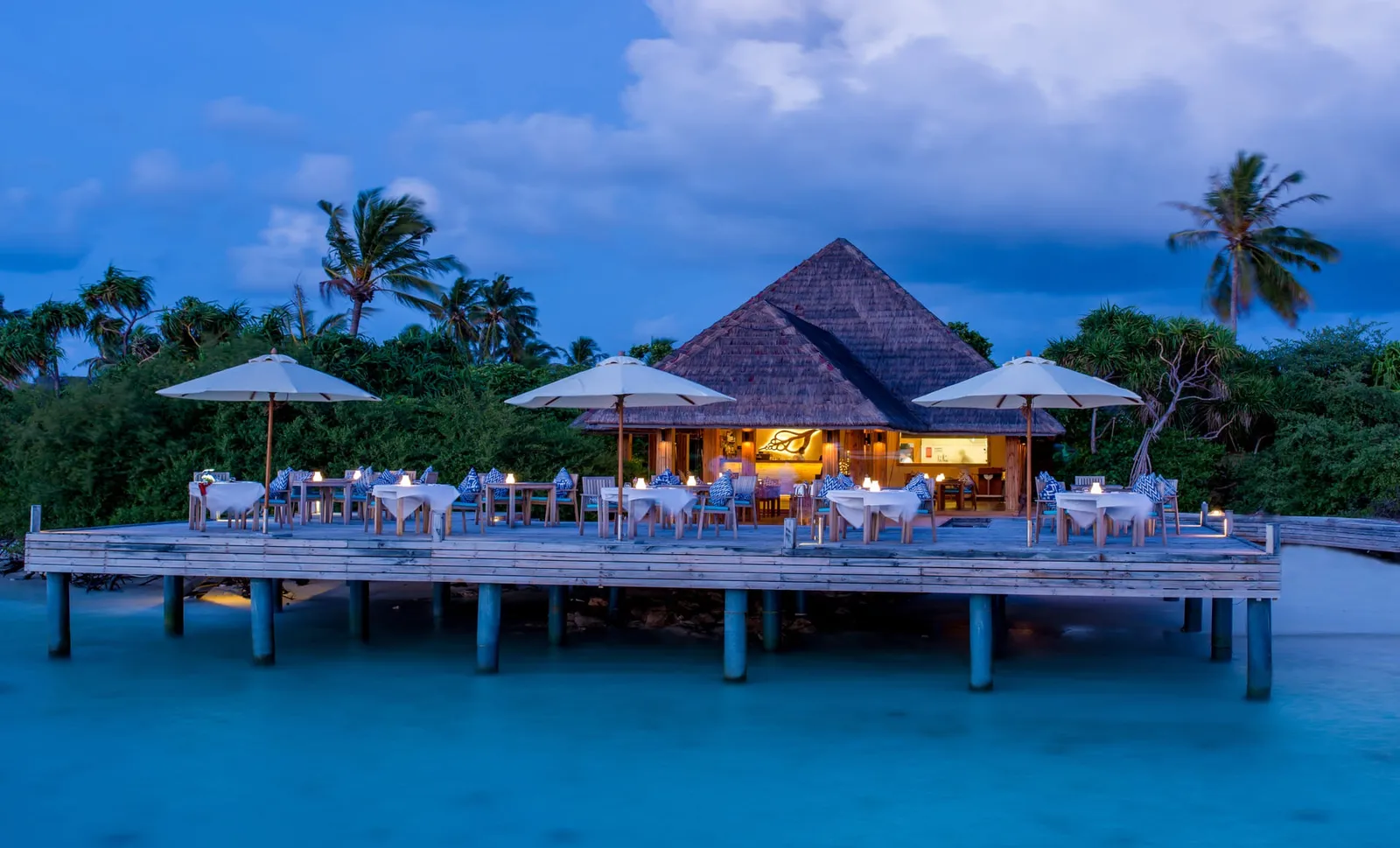 Sea Edge over the water at blue hour, its tables laid on the platform under parasols.