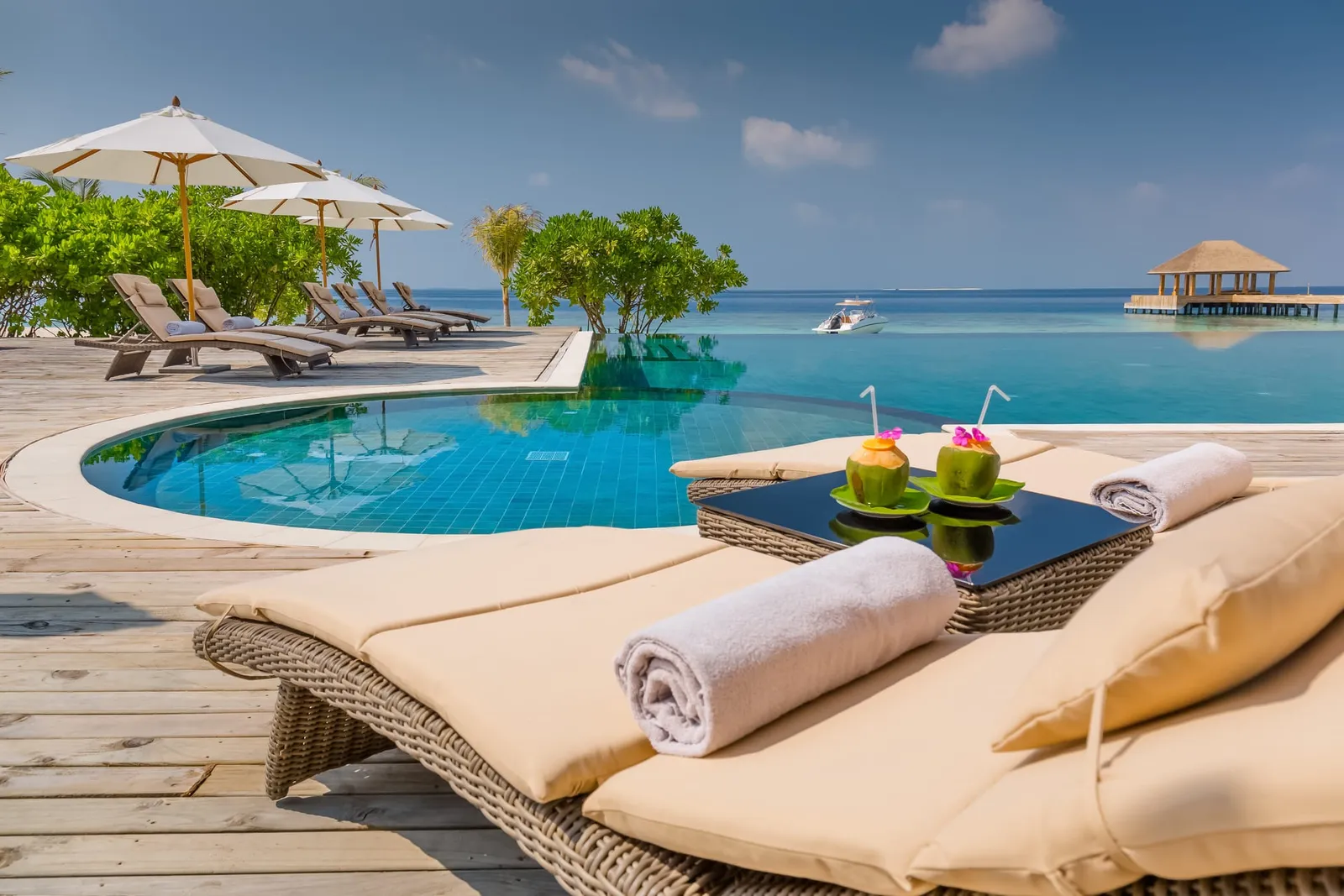 The edge of the Juju Bar infinity pool with its loungers, 2 coconuts on the table and the sea beyond the deck.