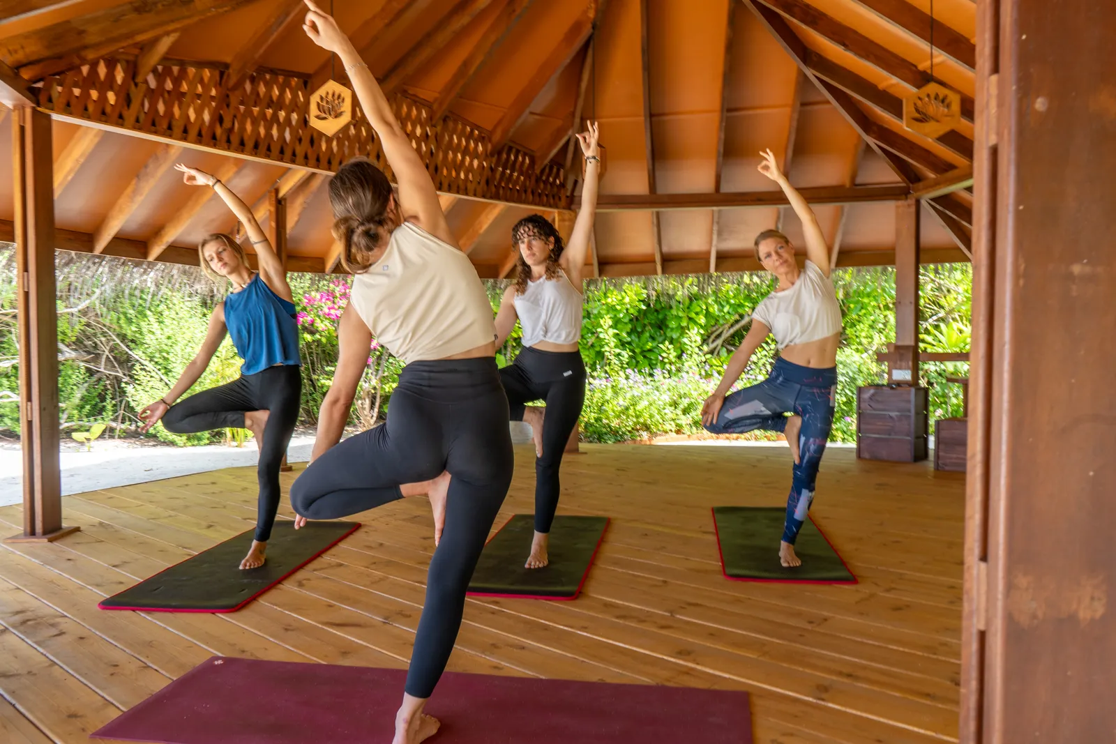 4 women balancing on one leg in the yoga pavilion, under its timber roof.