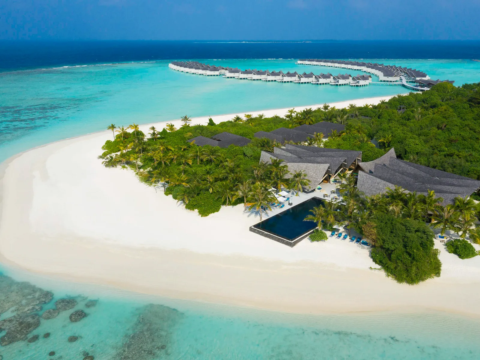 The island’s white sandspit from the air, the infinity pool and the overwater villas beyond