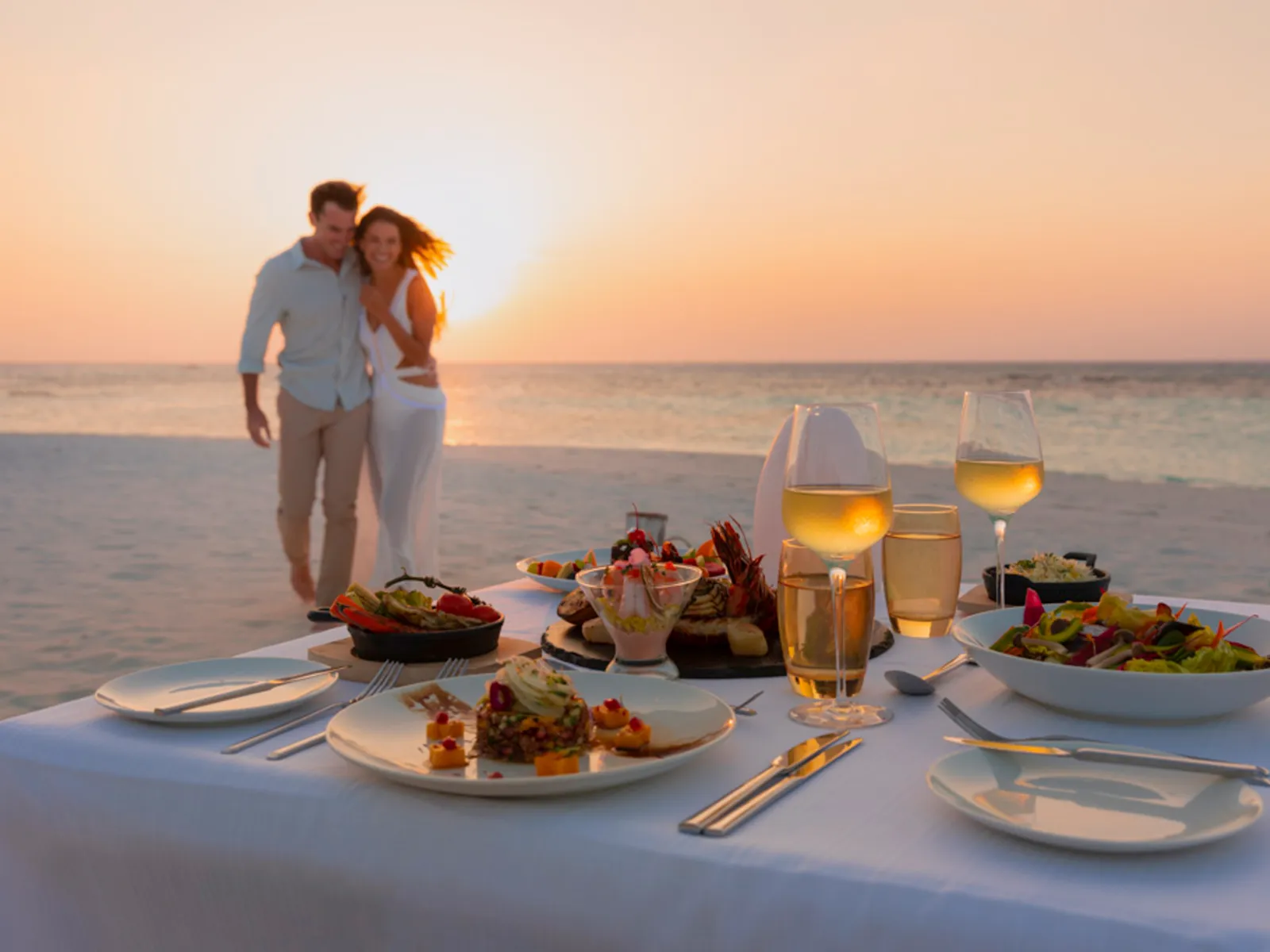 A couple dining on the beach at sunset, the table laid on the sand