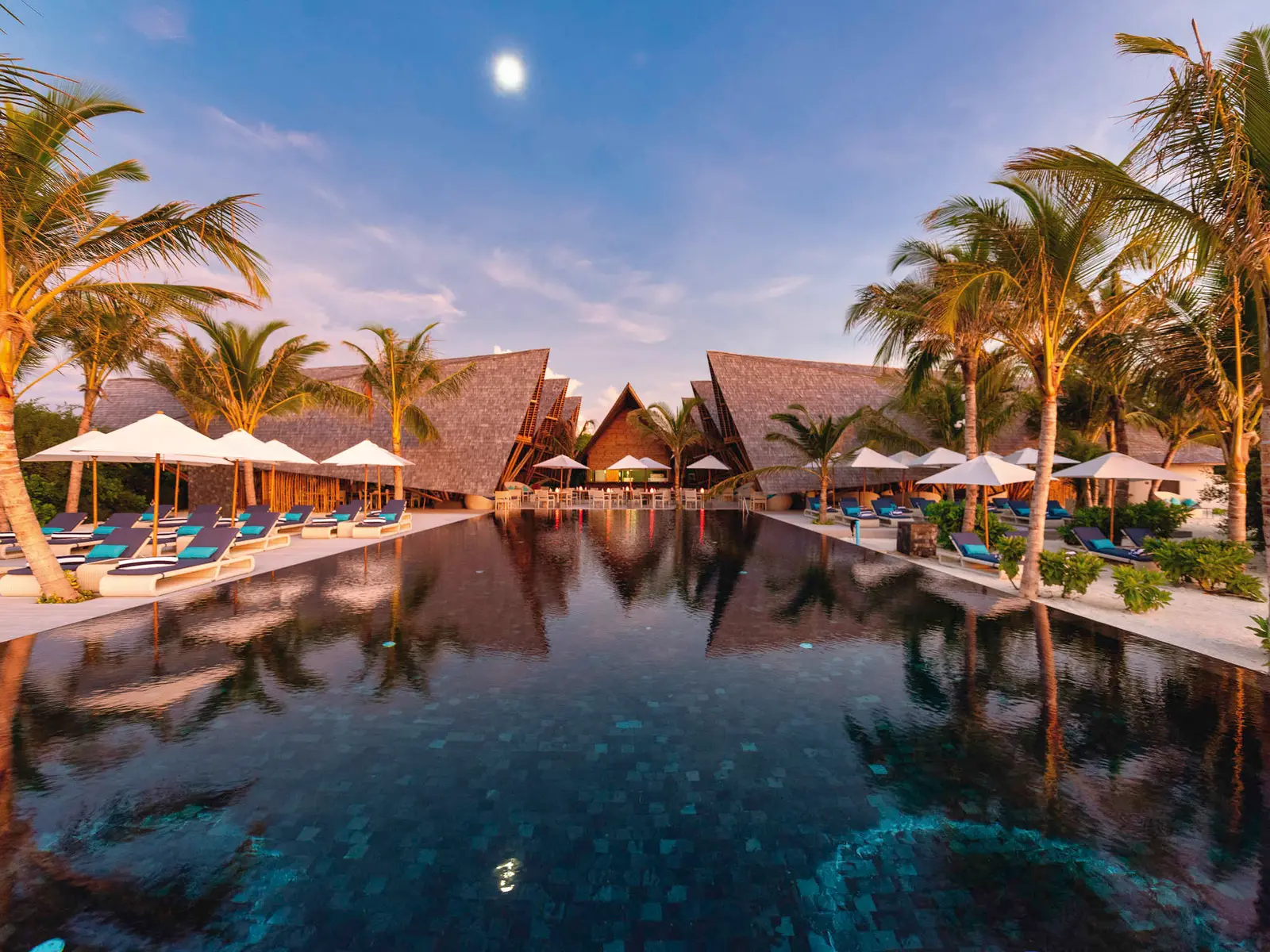 Latitude 5.5’s pool at dusk, palms and pointed roofs around it