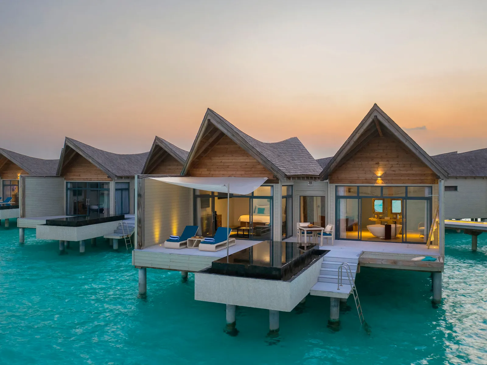 Overwater villas at sunset, lights on and steps down into the lagoon