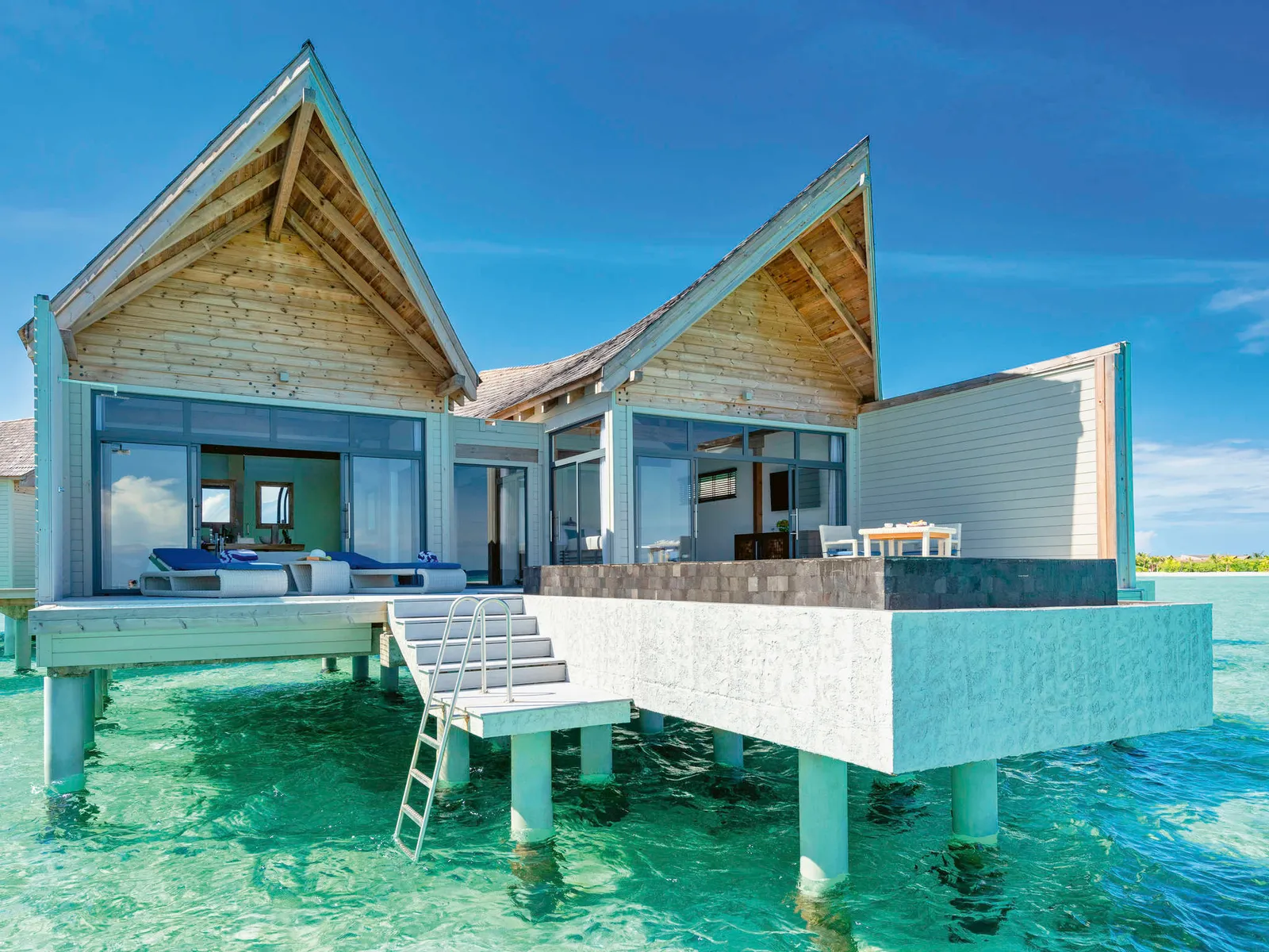 An overwater pool villa, its pointed roofs and ladder into the lagoon