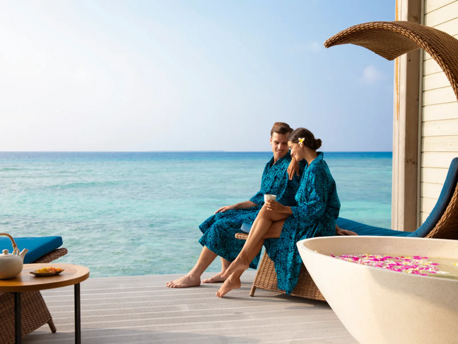 A couple in robes on the deck of an overwater spa suite