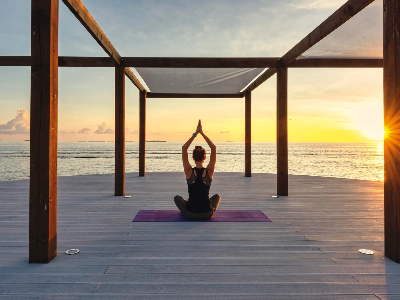 A woman meditating on the yoga pavilion, against the sunset
