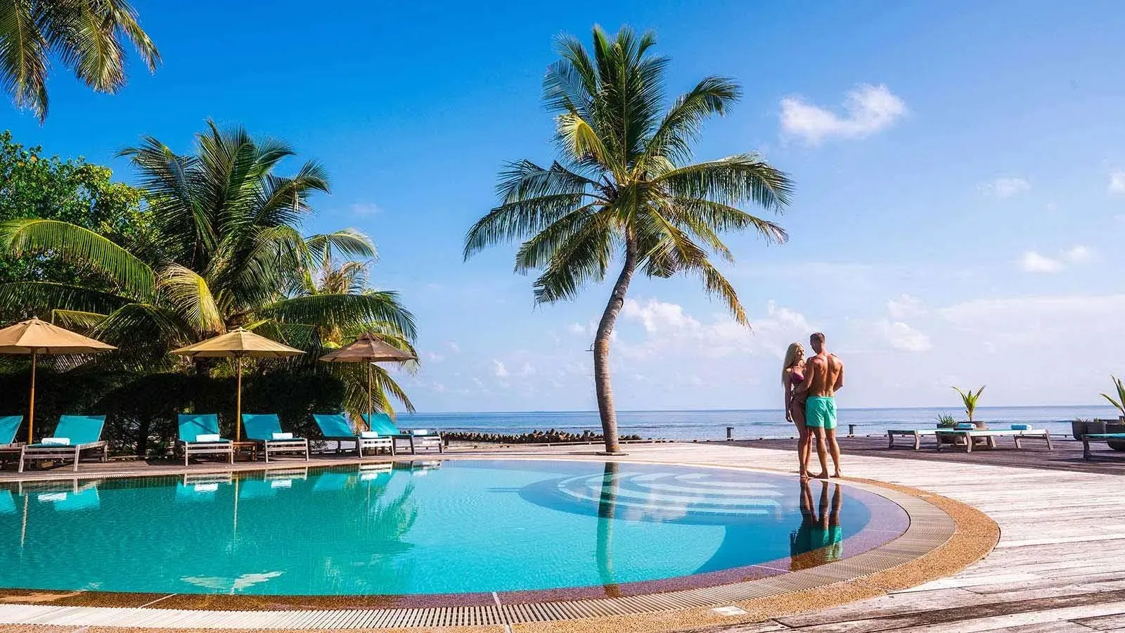 O Pool with 2 guests, palms and the sea behind