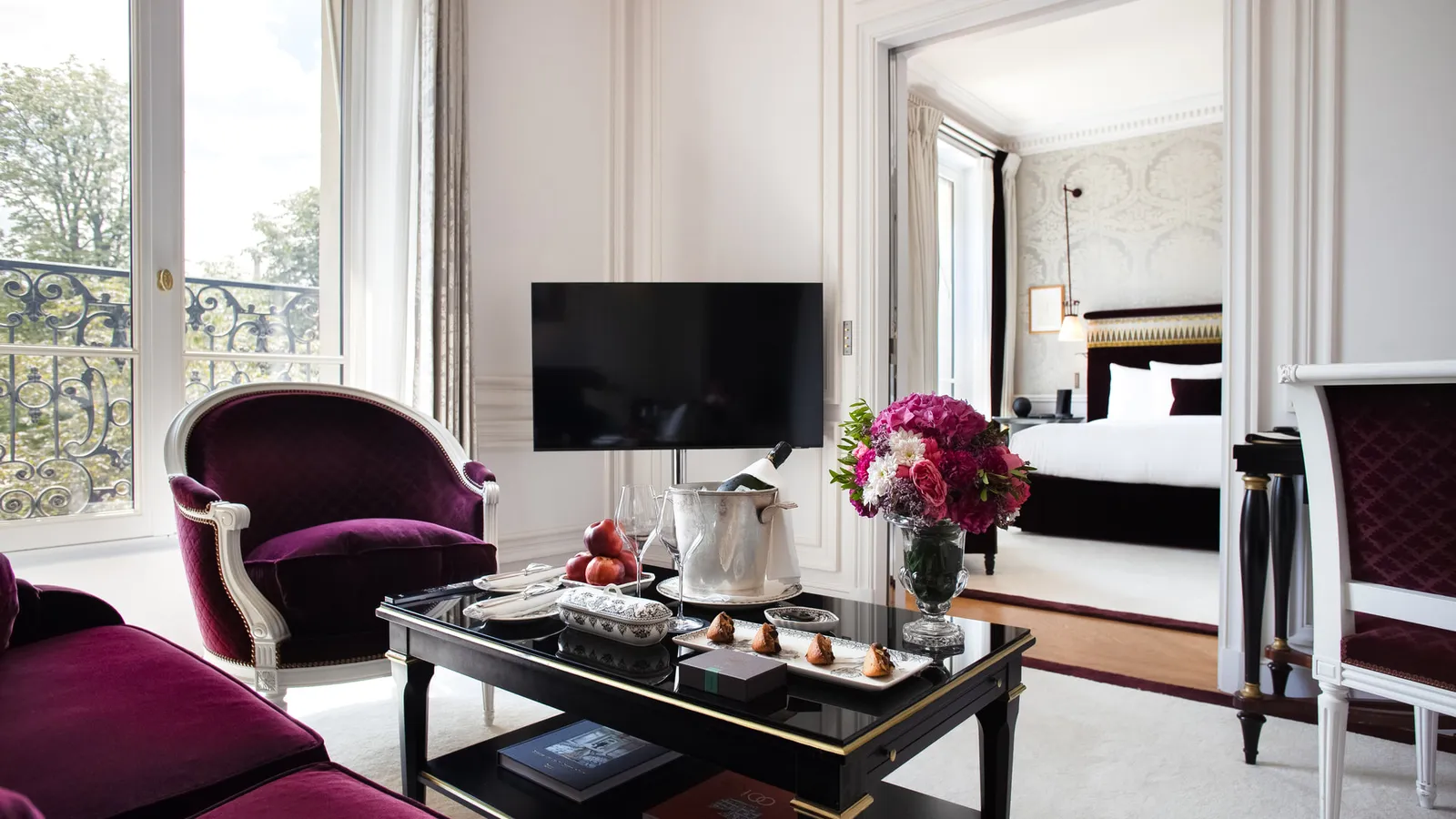 A sitting room with a purple armchair, dark desk and bedroom in the background