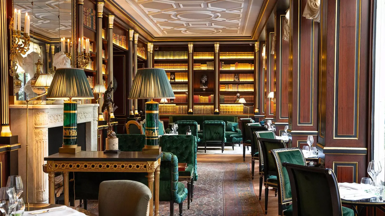 A library with wooden bookshelves, green armchairs and a fireplace
