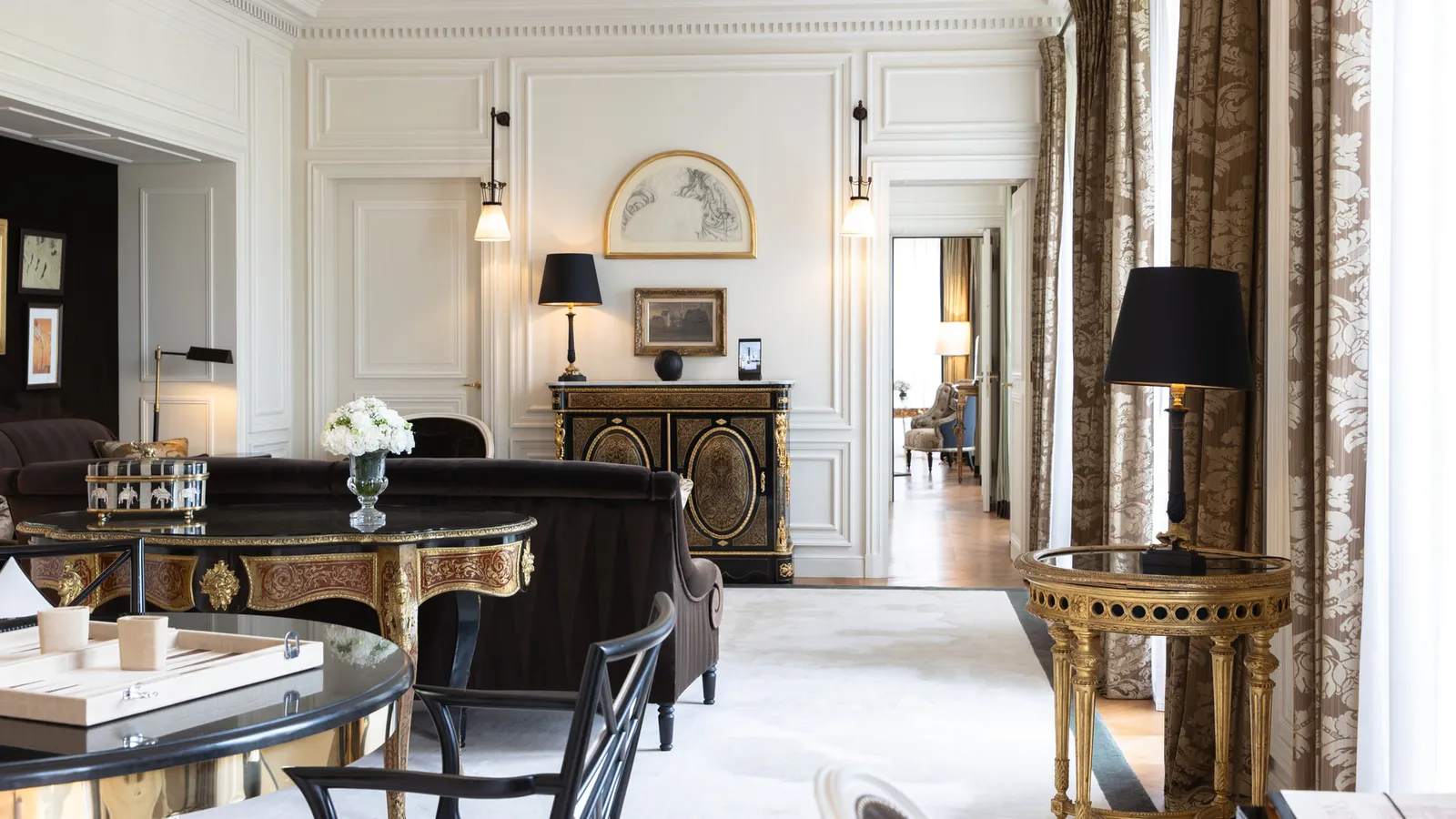 A sitting room with pale seating, gilded mirrors and windows