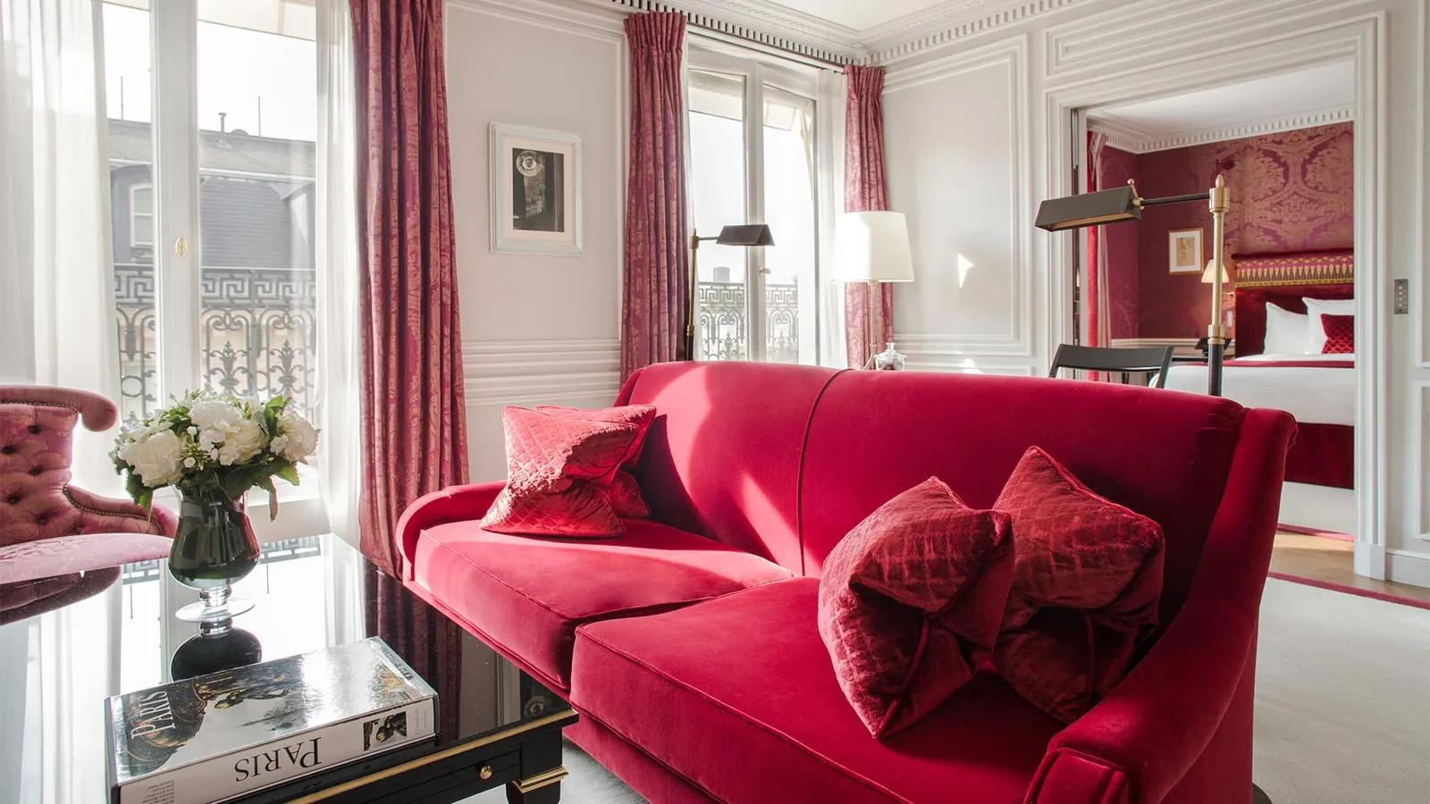 A sitting room with a red sofa and bedroom in the background