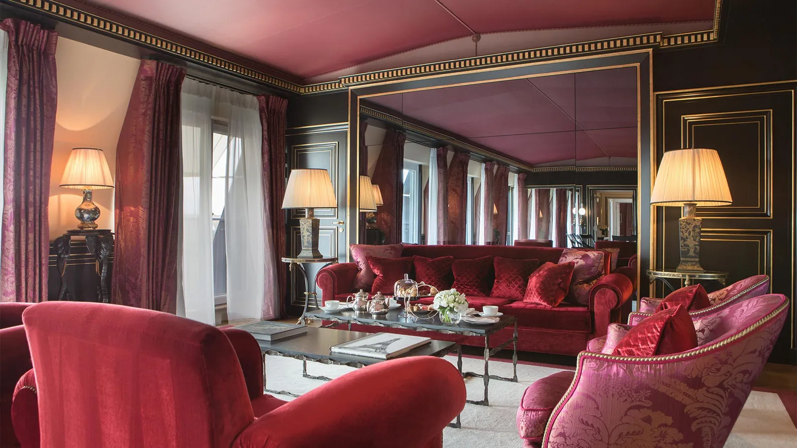 A sitting room with red seating, a coffee table and gilded details