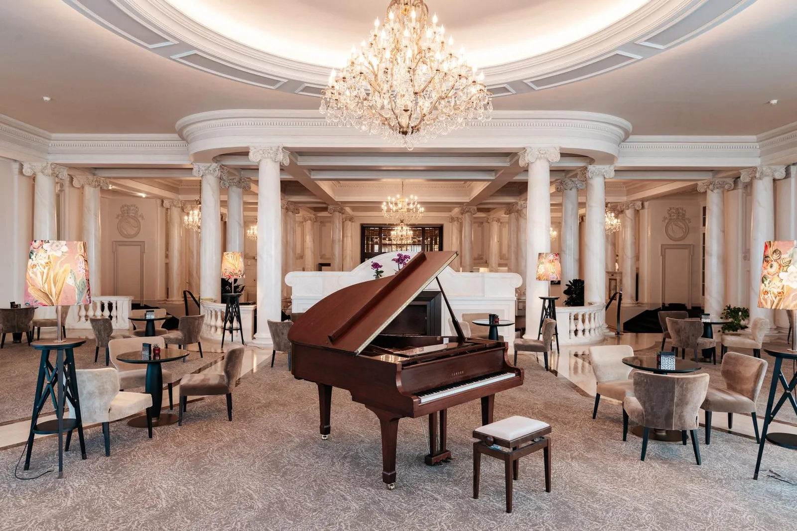 The lobby rotunda that houses Bar 1915: a grand piano beneath a large crystal chandelier, between white columns, with armchairs and small tables