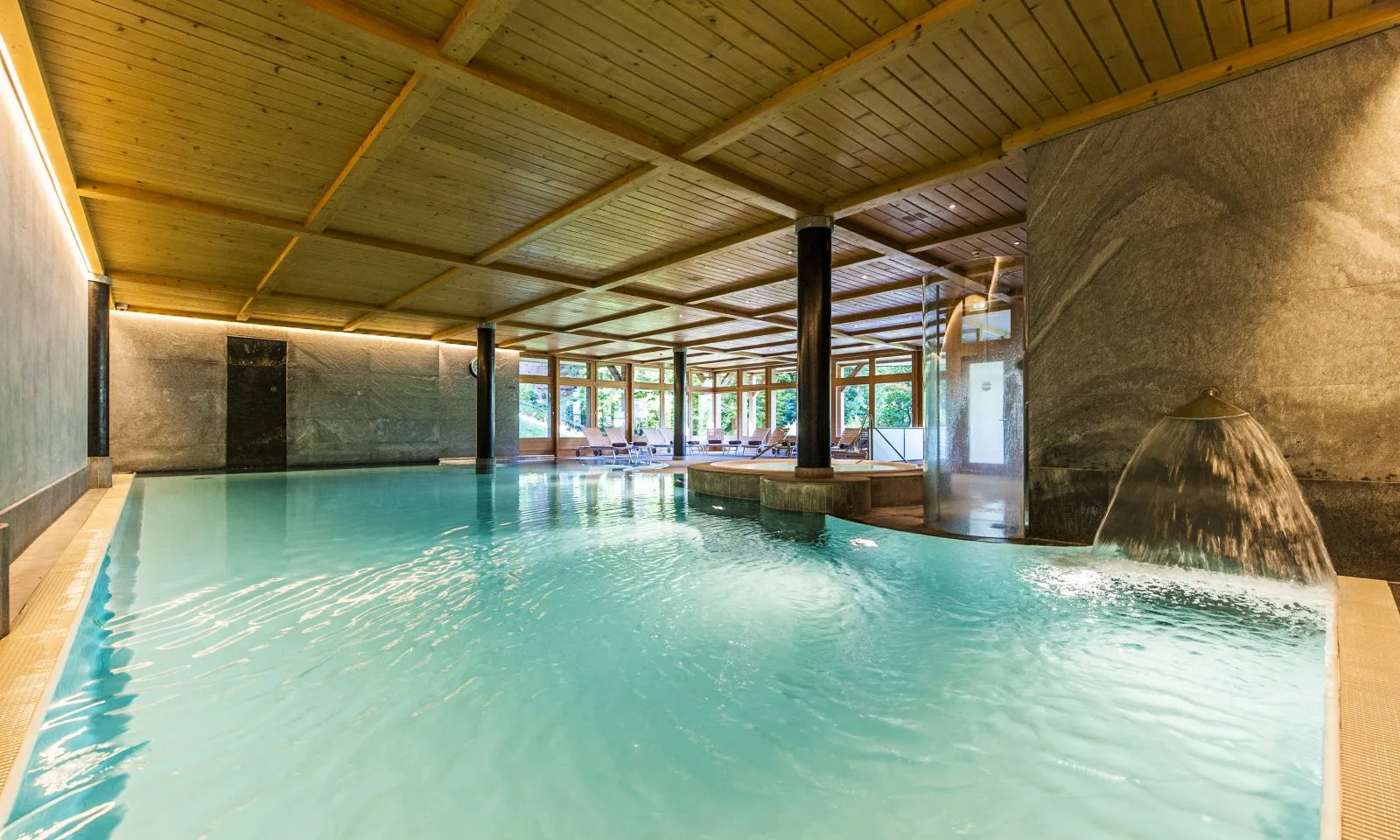 La piscina interna con il soffitto di legno e le vetrate sul giardino