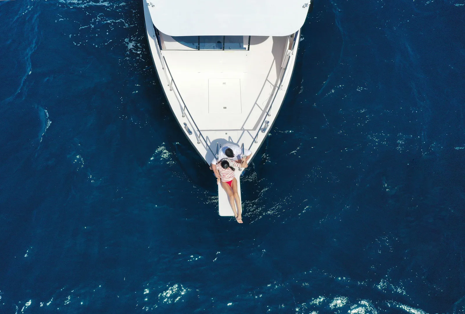 A boat’s bow from above, a couple lying out over the deep blue sea