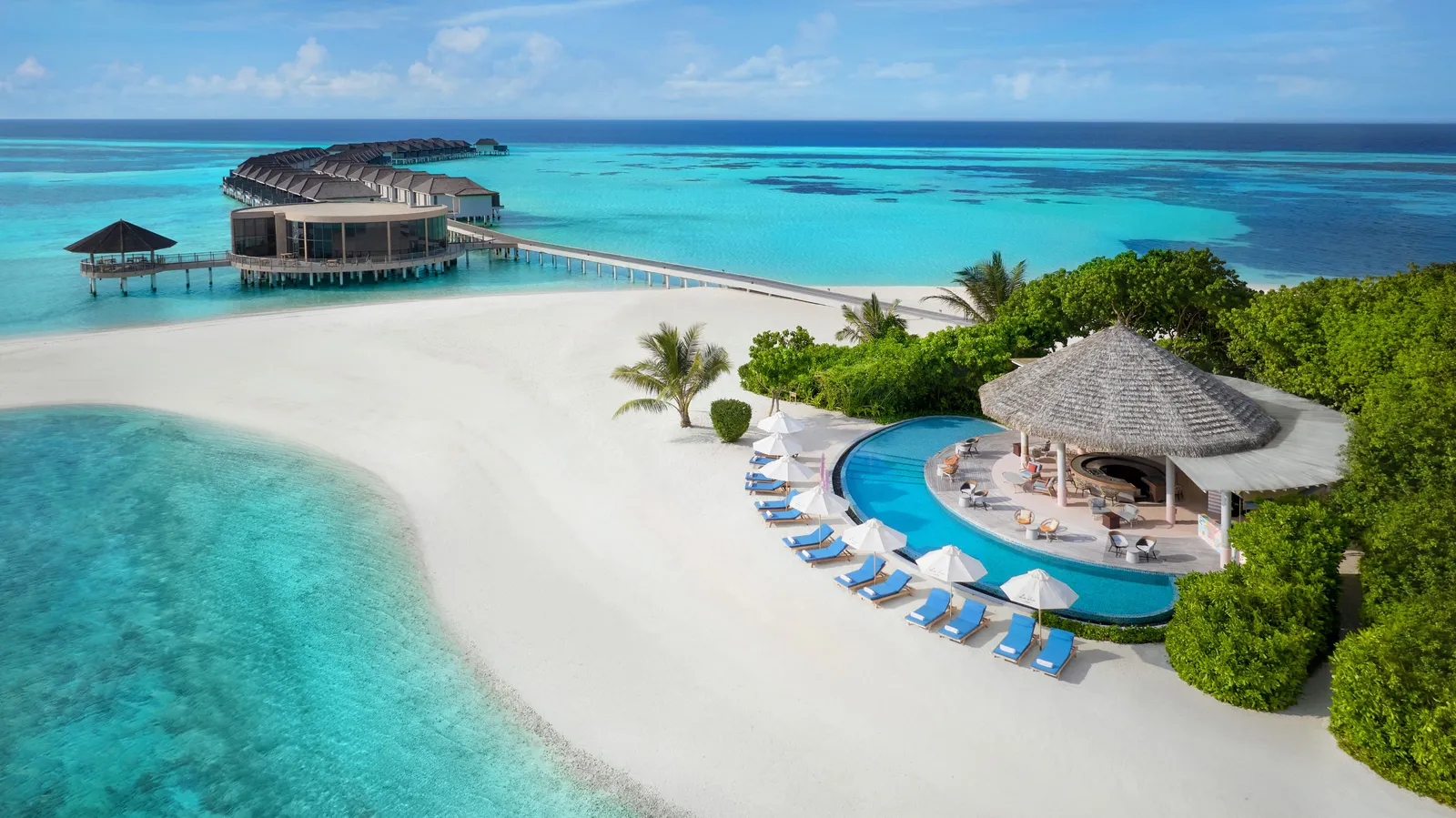 The beach and a bar’s round pool among the palms, the overwater villas beyond
