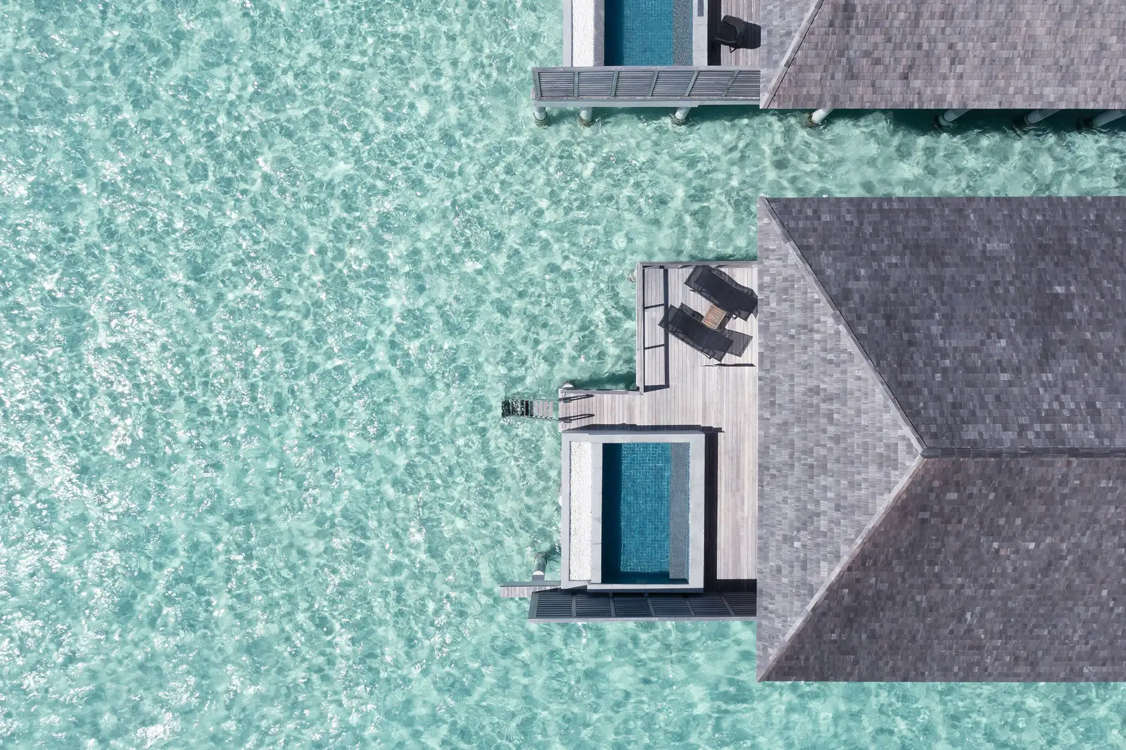 An overwater pool villa from above, its deck and pool over the lagoon